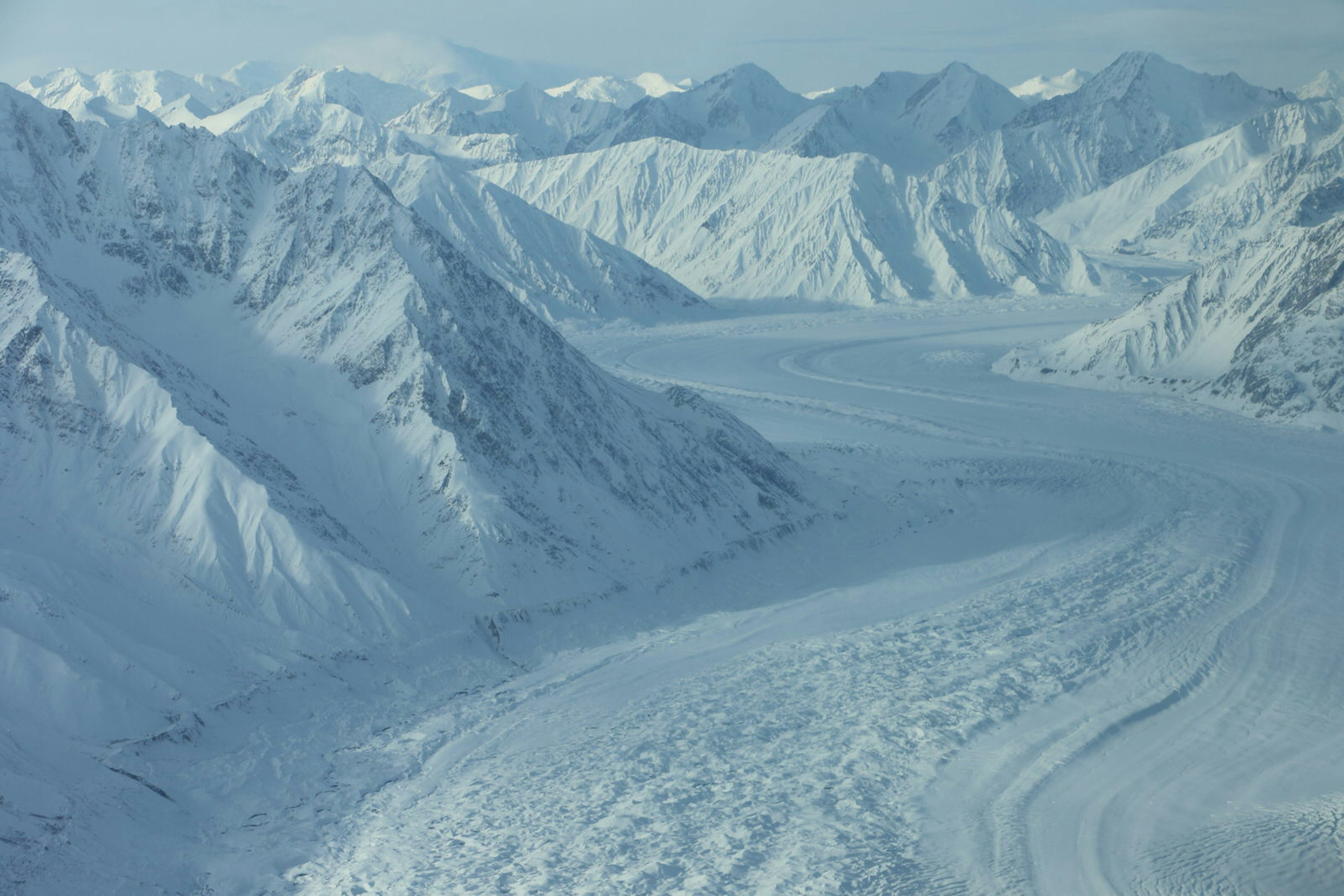 A river of ice fills the space between two sets of snow covered mountains, as seen from a small aircraft © Mike MacEacheran / Lonely Planet