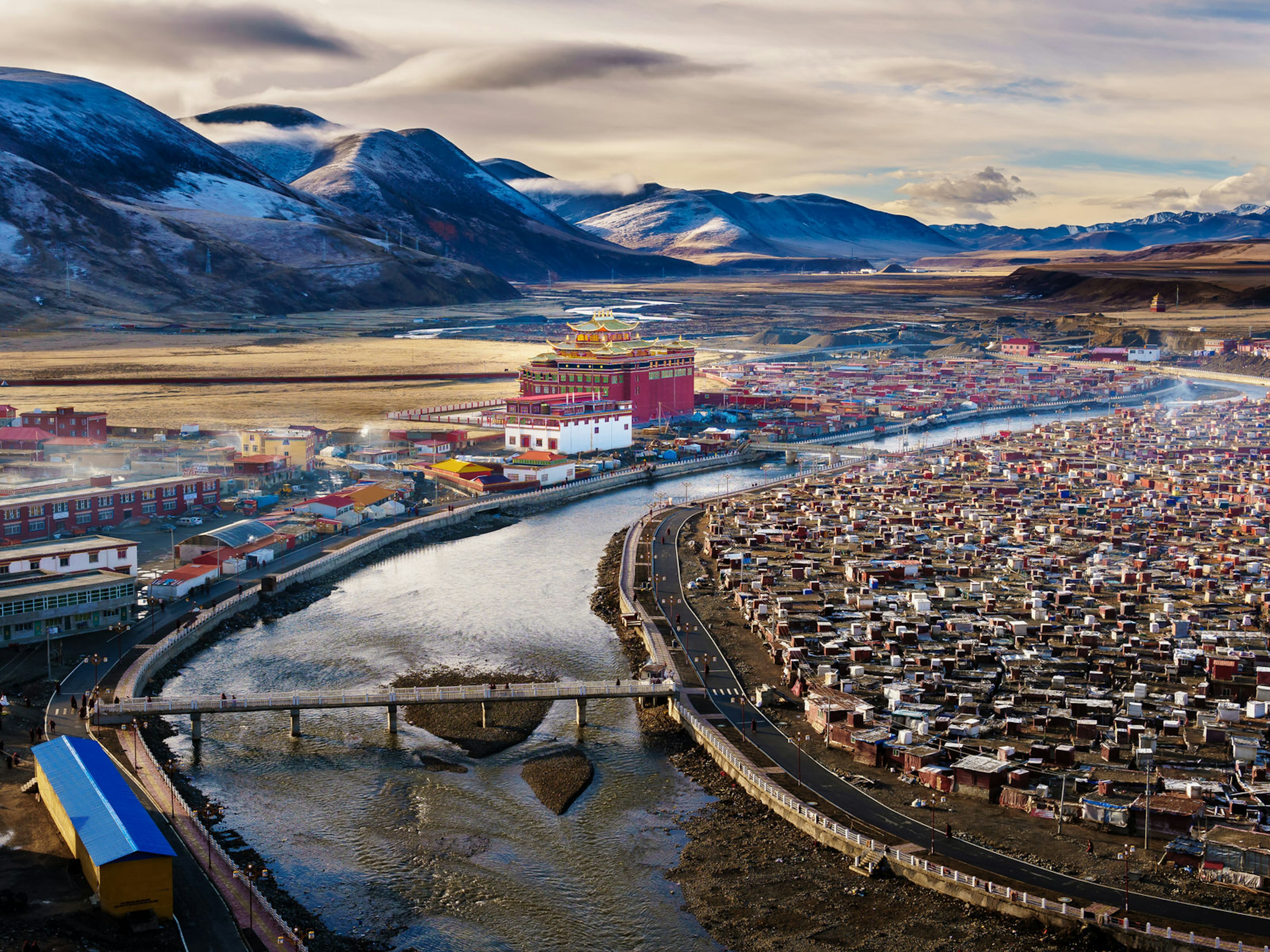 Aerial view of Yarchen Gar, with monastery buildings along a bend in a river and snowy mountains in the background. Some 10,000 monastics live at Tibetan Buddhist Yarchen Gar in Western Sichuan's Garzi Prefecture ? DavidWebb / Shutterstock