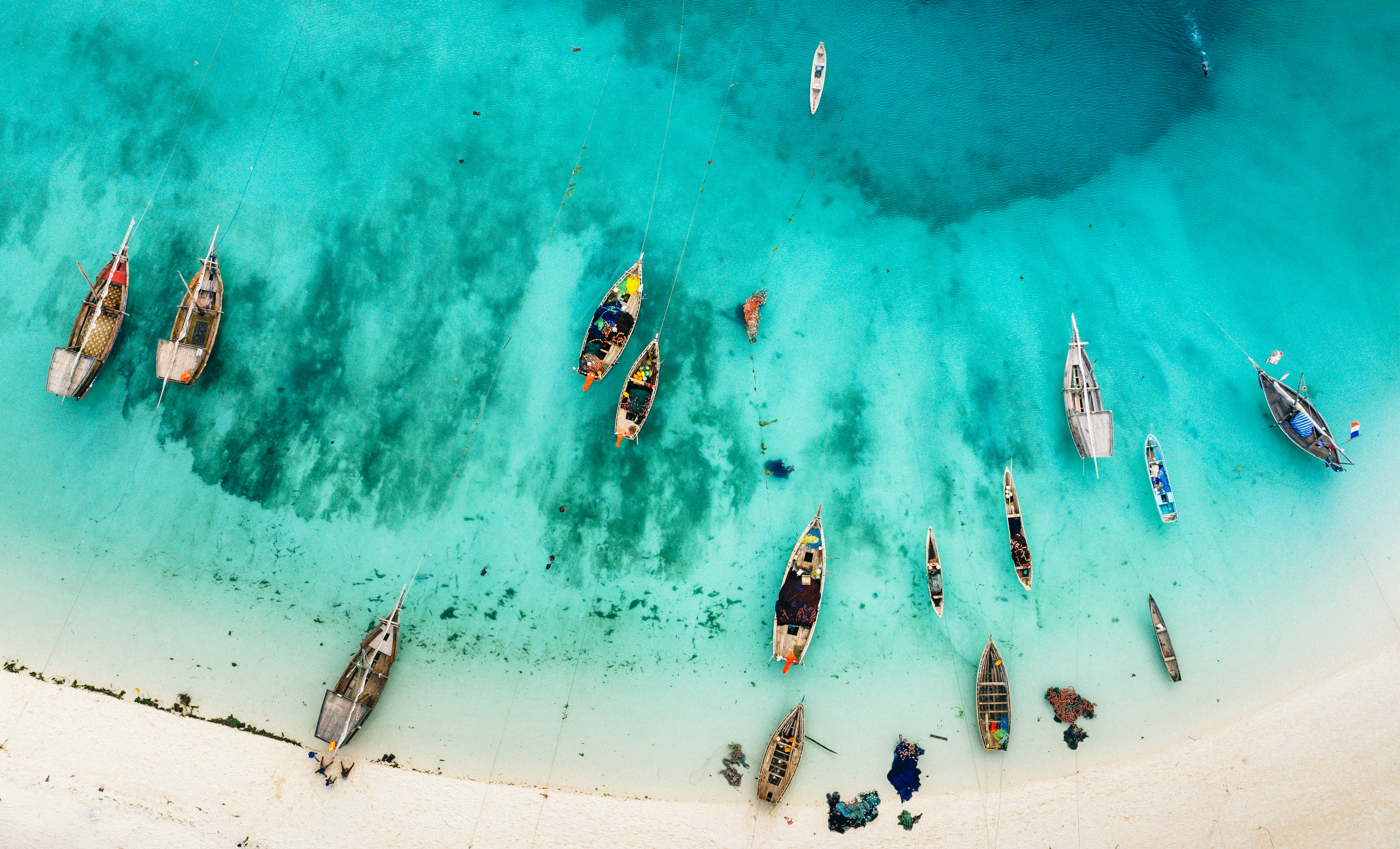 A drone shot shows the crystal blue waters and boats at a beach in Zanzibar.