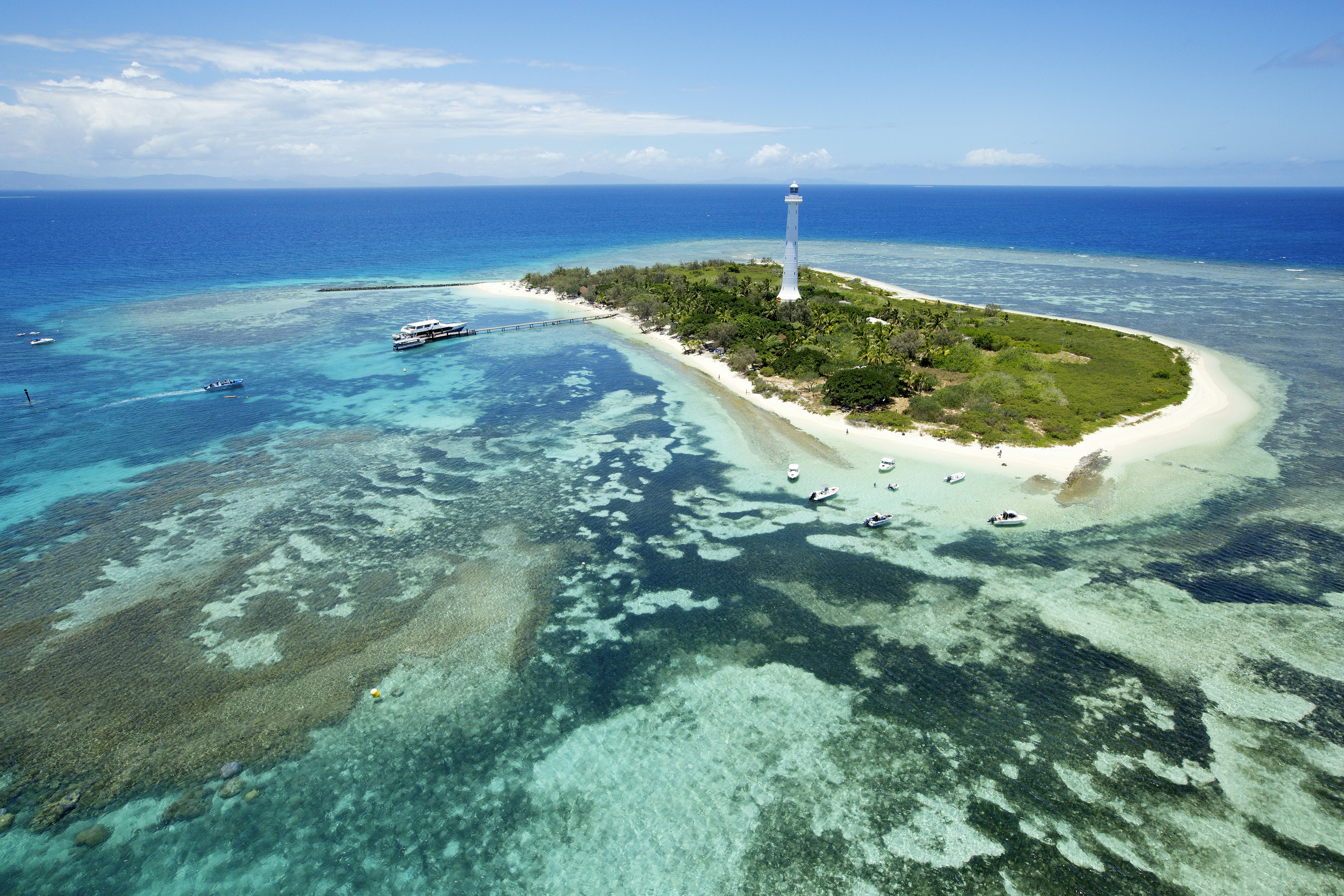 The Amedee Lighthouse stands tall and white on a tiny green island called the Moumea nature reserve that's almost flat and surroudned by white sand beaches the descend into shallow, translucent blue waters of the surrounding lagoon