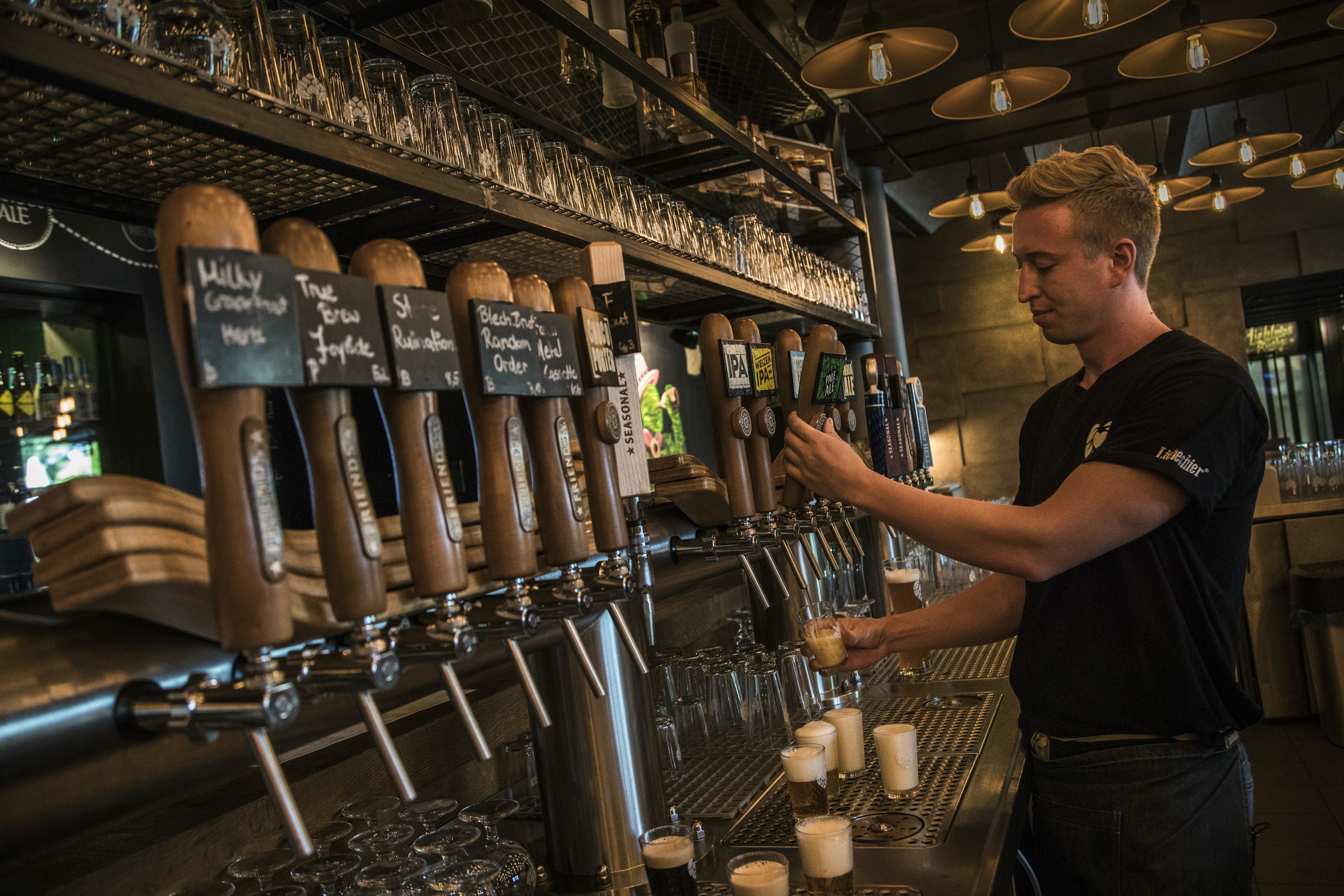 A bartender in Germany pulls a pint of beer from a row of wooden taps inside a cozy pub