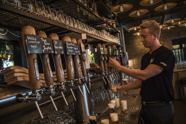 A bartender in Germany pulls a pint of beer from a row of wooden taps inside a cozy pub