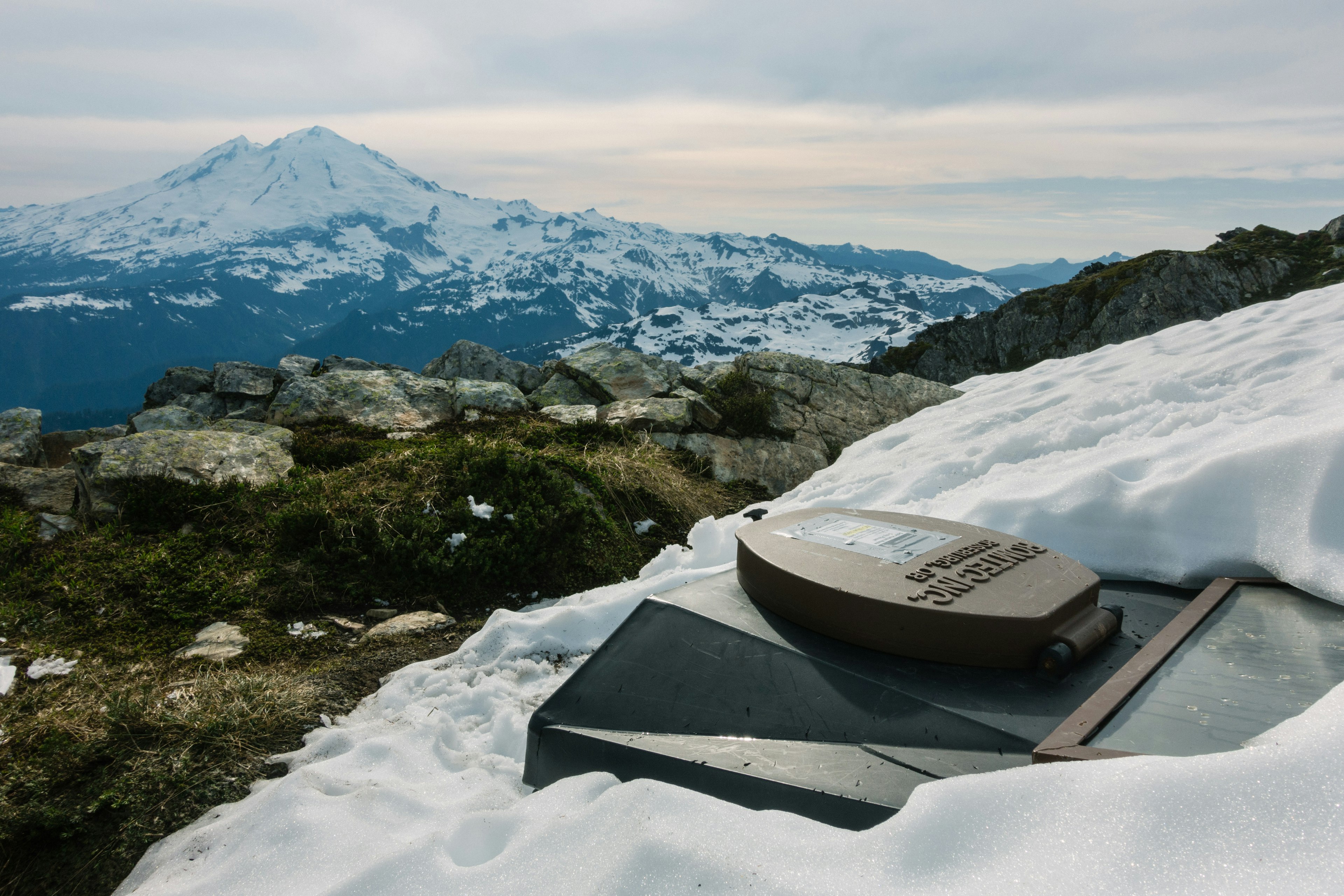 A toilet buried in a snowbank overlooking a mountain.