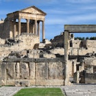 Looking very much like the Forum in Rome, this image is filled with stone ruins; rising into the blue sky at the back of the image is Roman temple with its front facade still held high by six large columns.