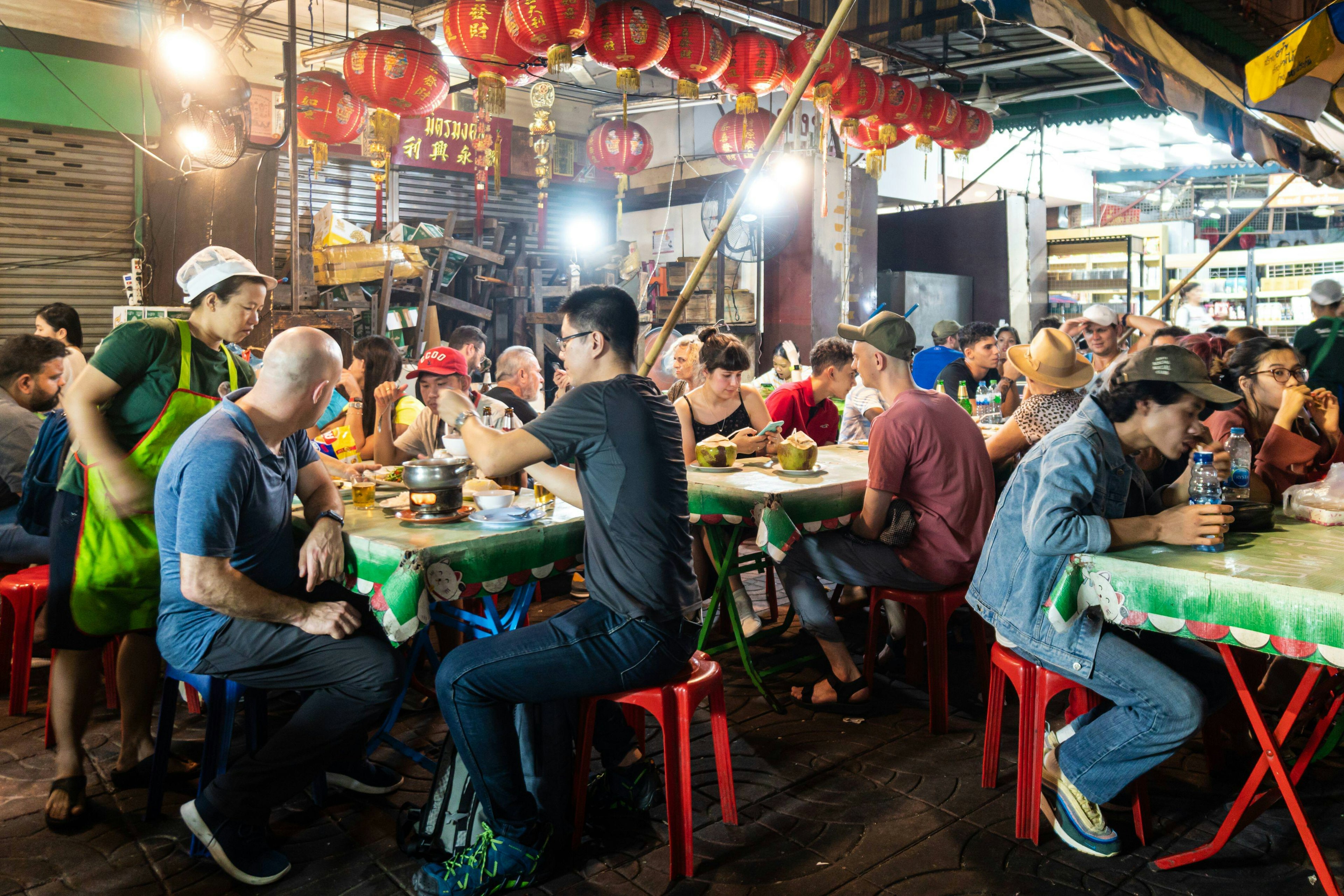 People sit at tables eating street food at a casual restaurant around Yaowarat St at night, Chinatown, Bangkok, Thailand