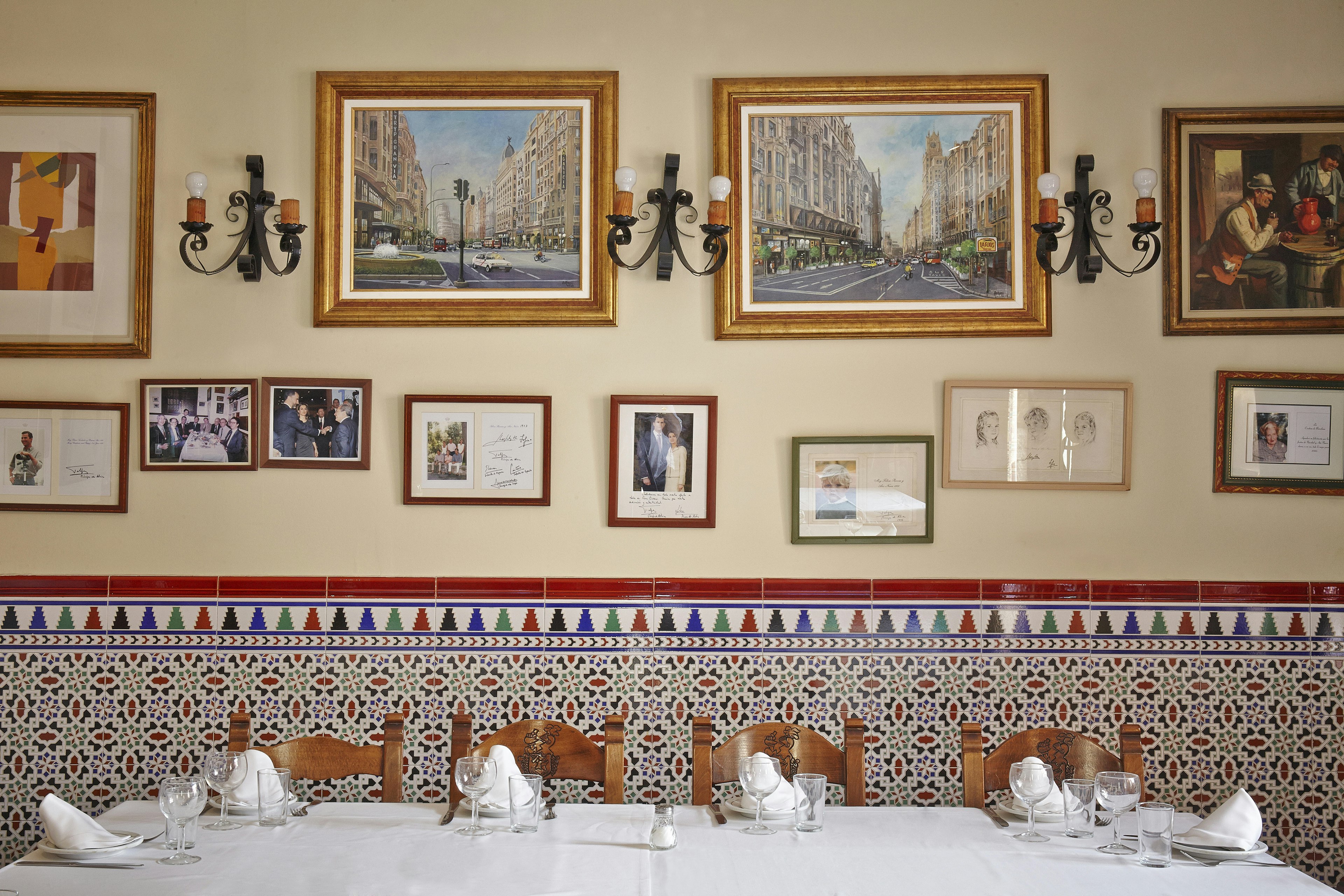 The interior of Casa Ciriaco in Madrid: many historic photos line the walls, and there are dark wood chairs and white tablecloths.