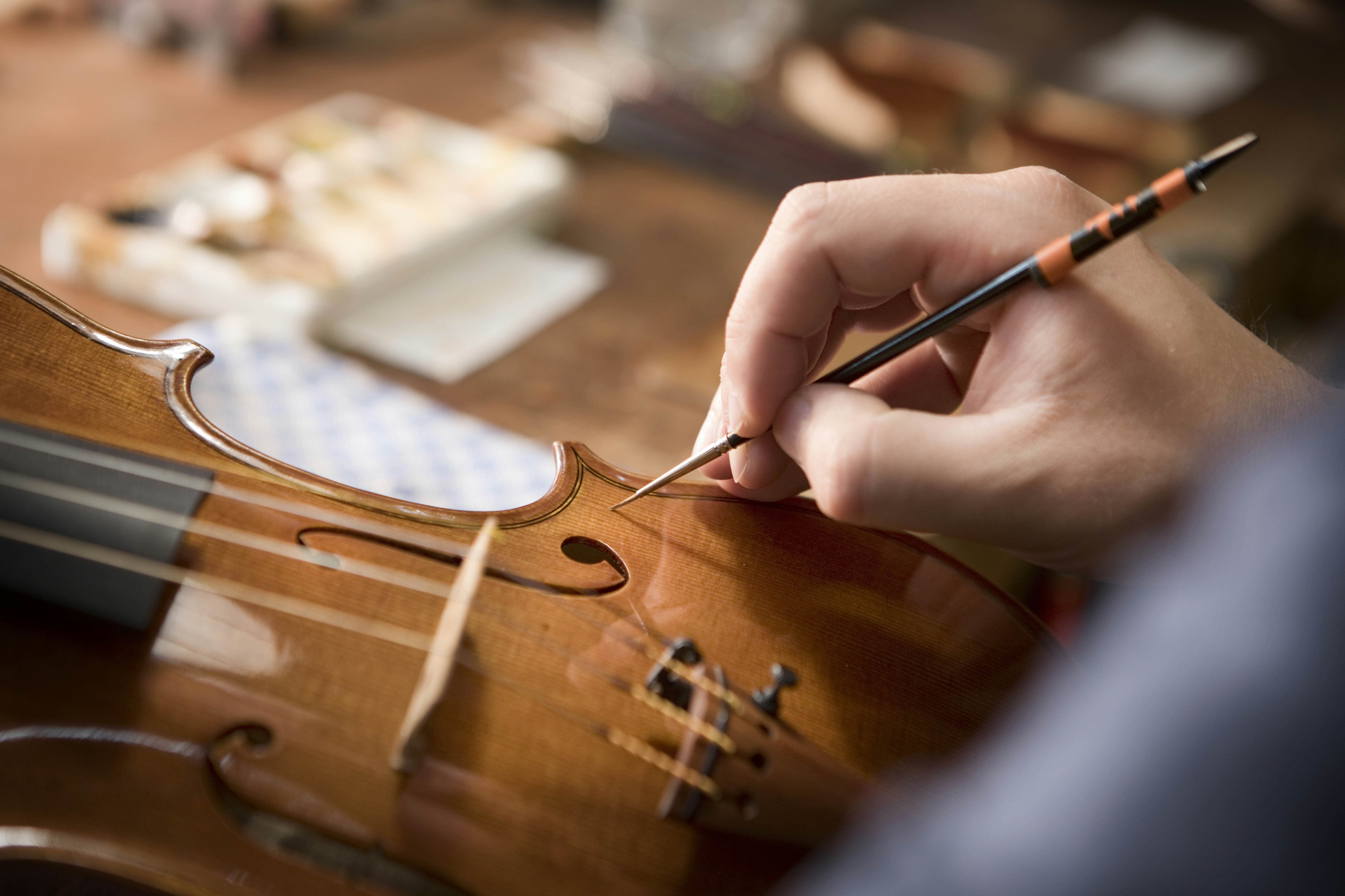 In a close-up, a hand delicately paints a stain or clear coat onto a hand-crafted violin in Füssen, Germany