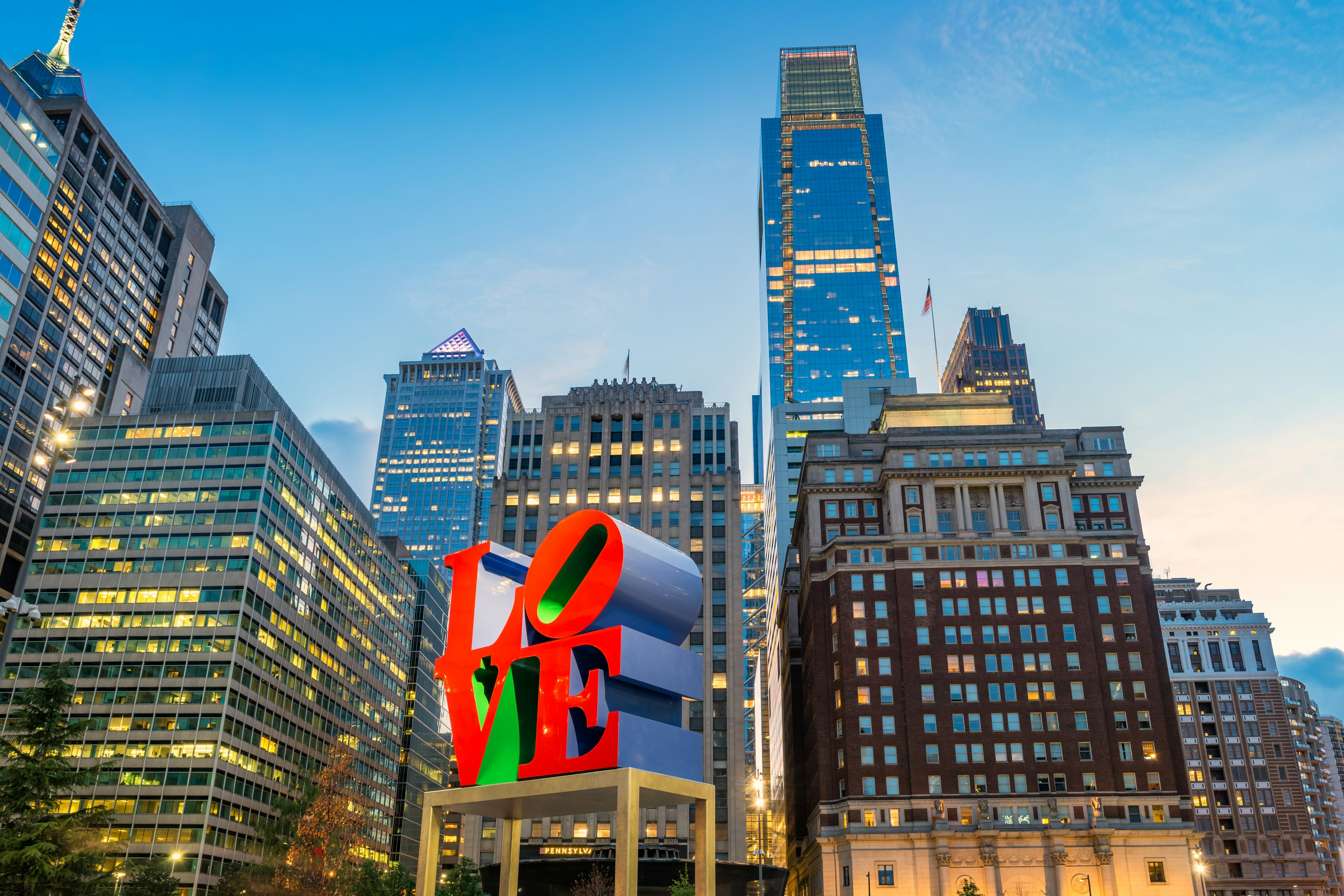 A large red sculpture spelling out "LOVE" in the center of a city square with high-rise buidlings all around