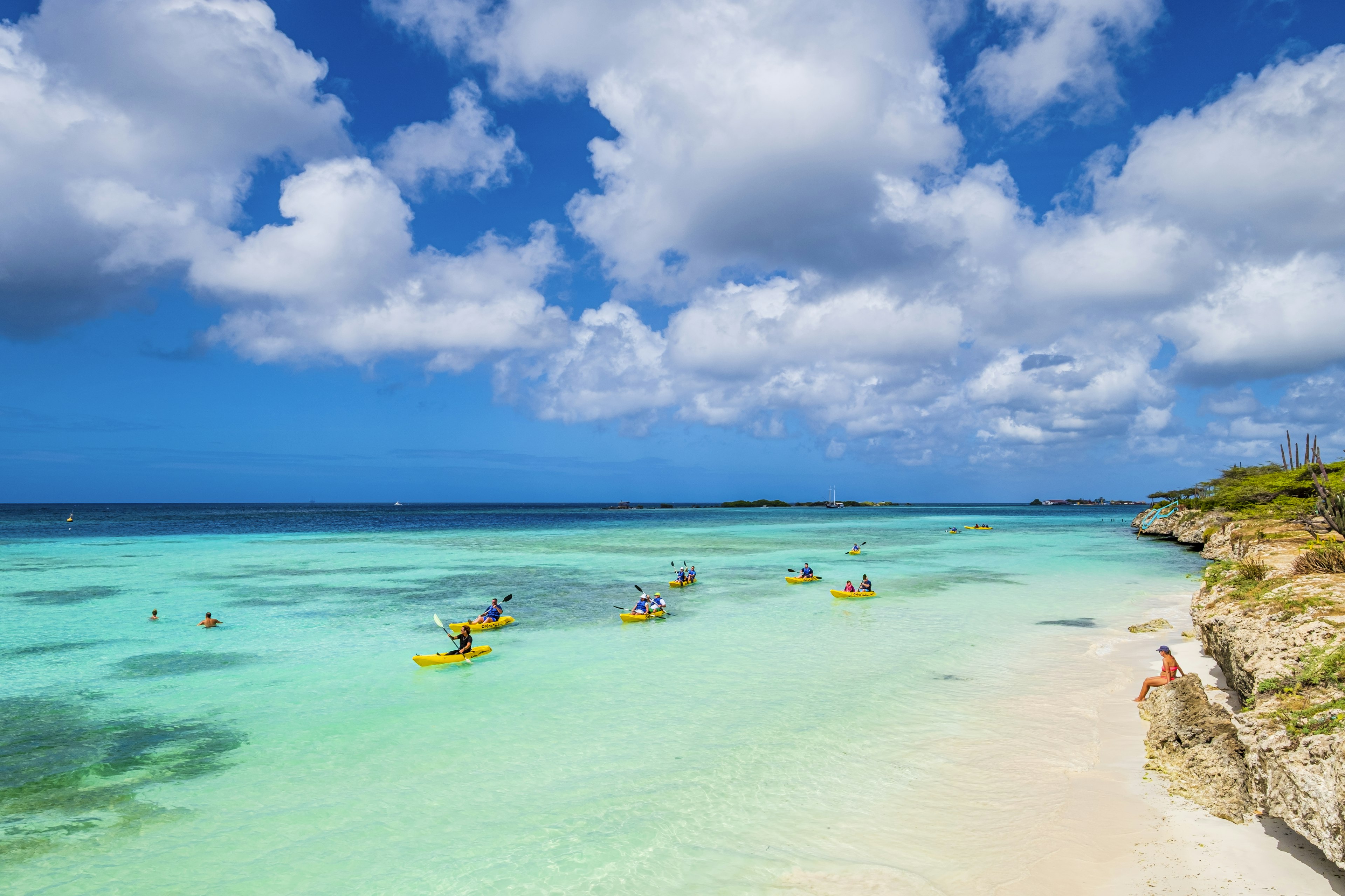 Kayakers in yellow kayaks paddle over beautiful clear blue waters