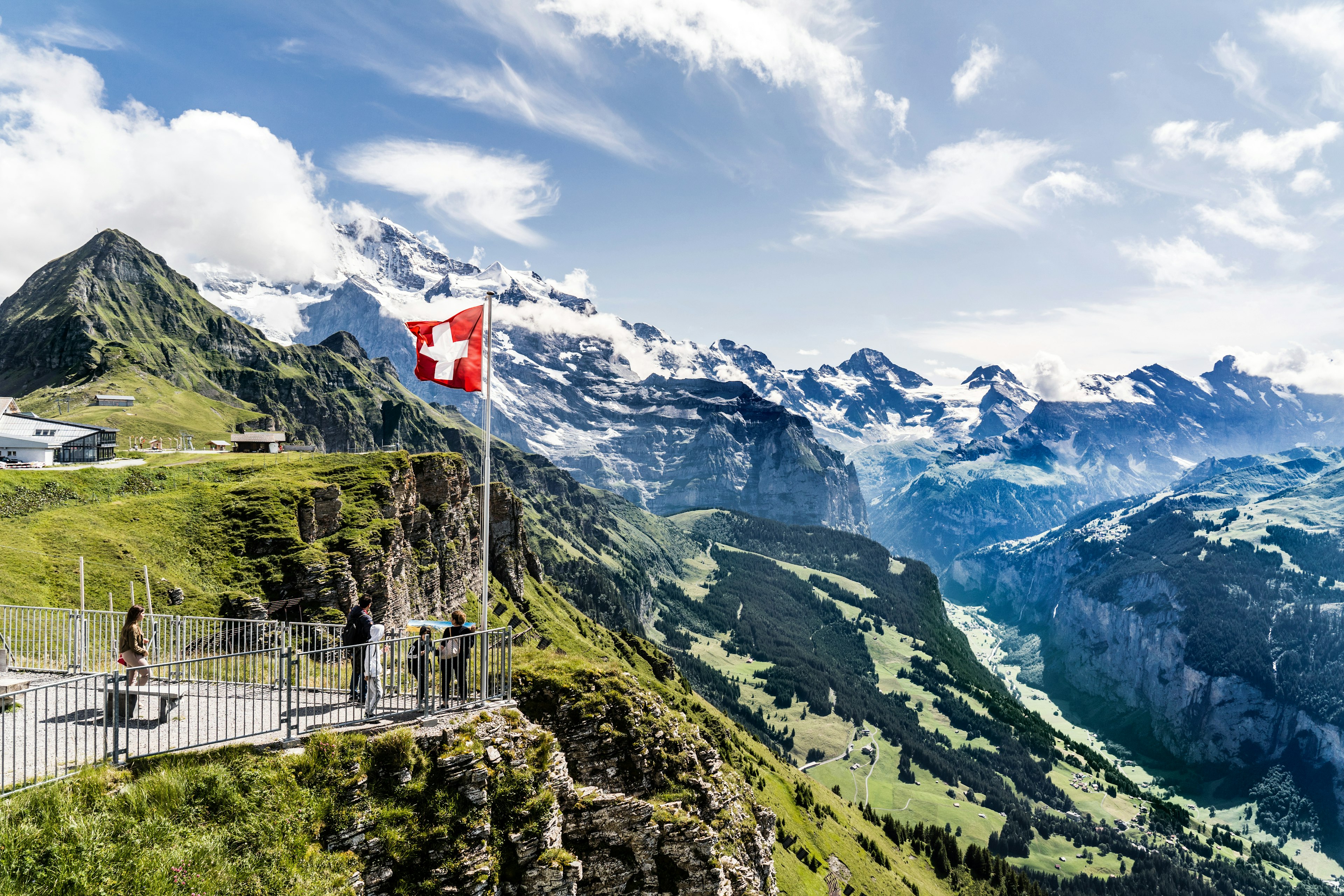 A family stand at a mountain viewing platform with the red and white Swiss flag flying above them