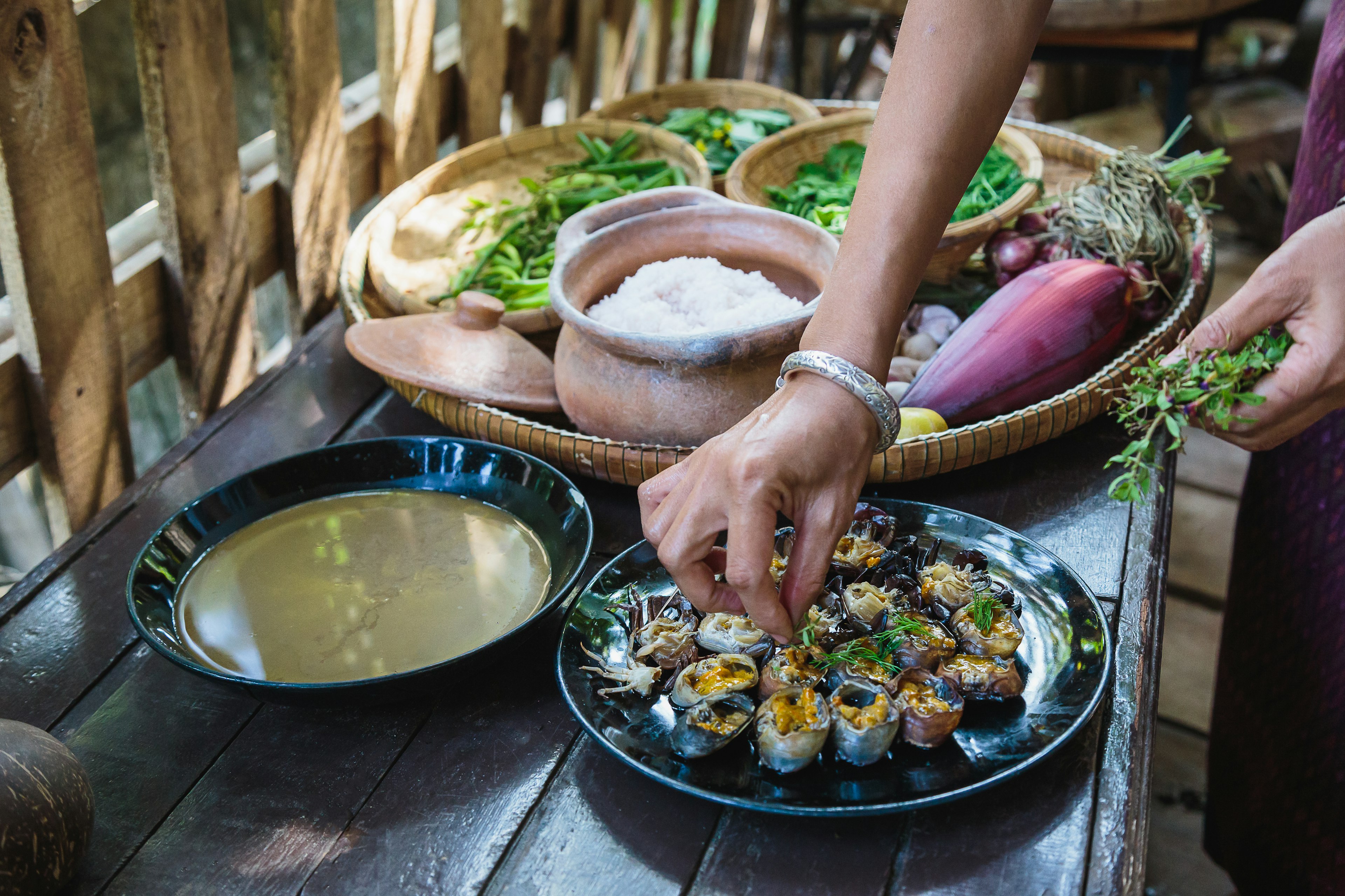 The hand of a woman preparing and cooking homemade grilled field crabs and vegetables at a traditional Thai kitchen in Isan, Northeast Thailand