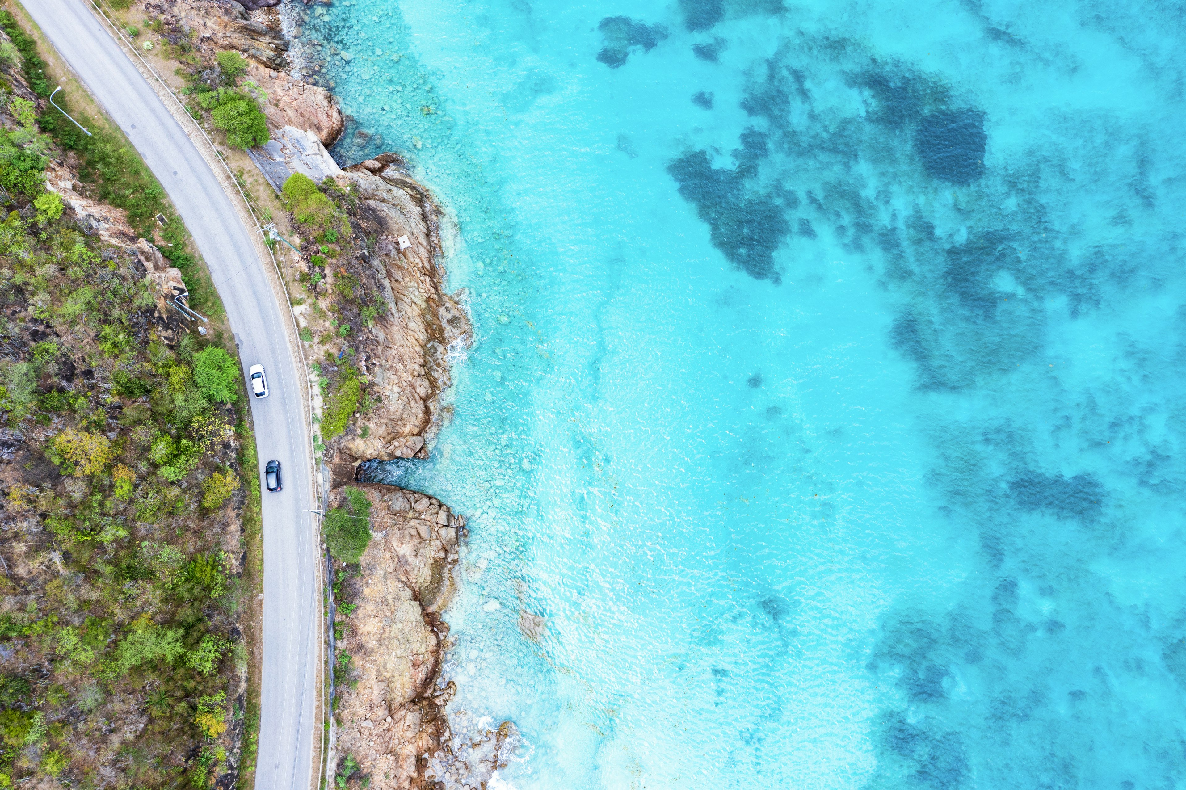 Aerial view of cars driving on road beside the turquoise crystal sea, Antigua, Caribbean, West Indies