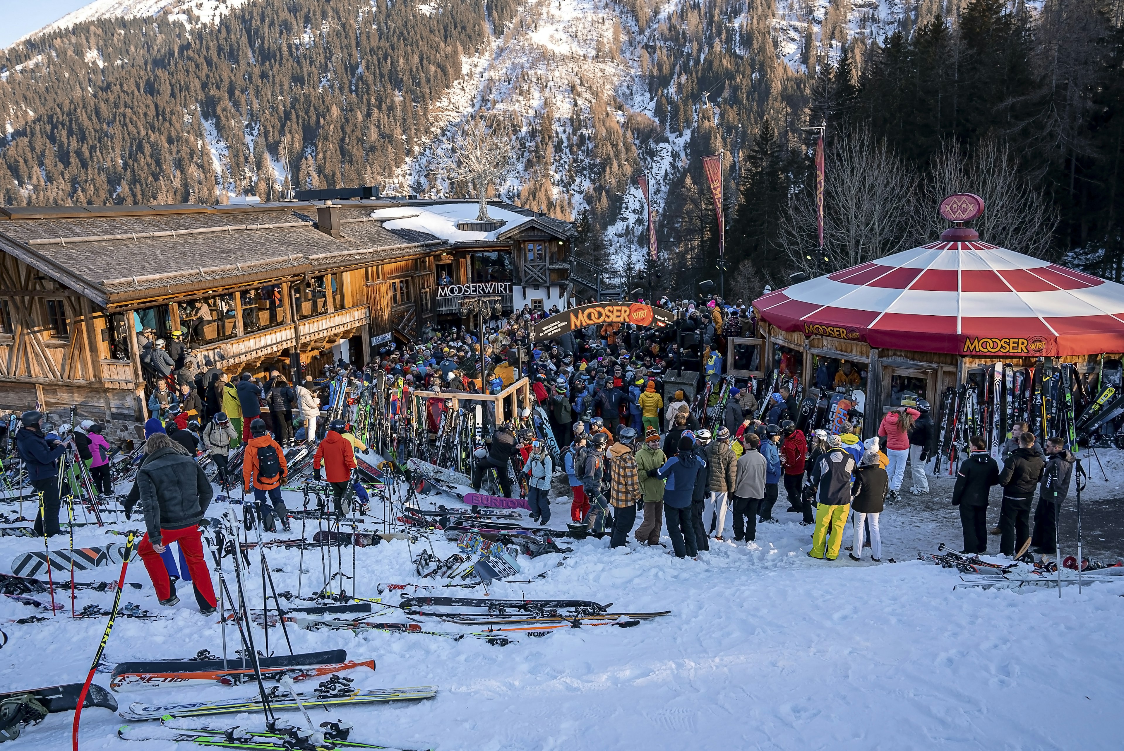 A large group of skiers waiting outside a chalet-style bar right on the slopes