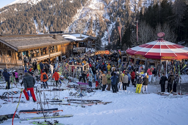 A large group of skiers waiting outside a chalet-style bar right on the slopes