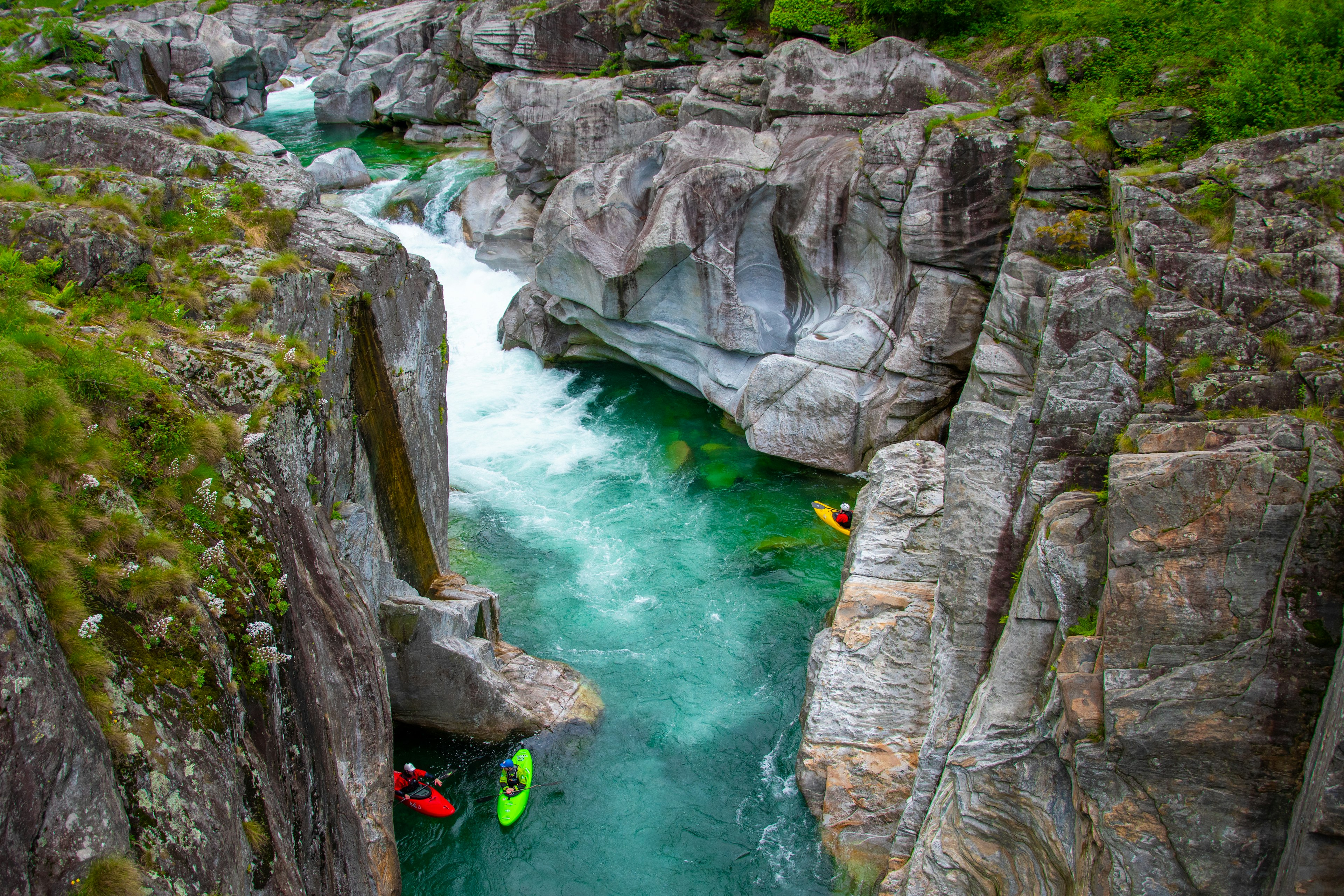 An aerial shot of three brightly colored kayaks on the fast-flowing water of the Val Verzasca