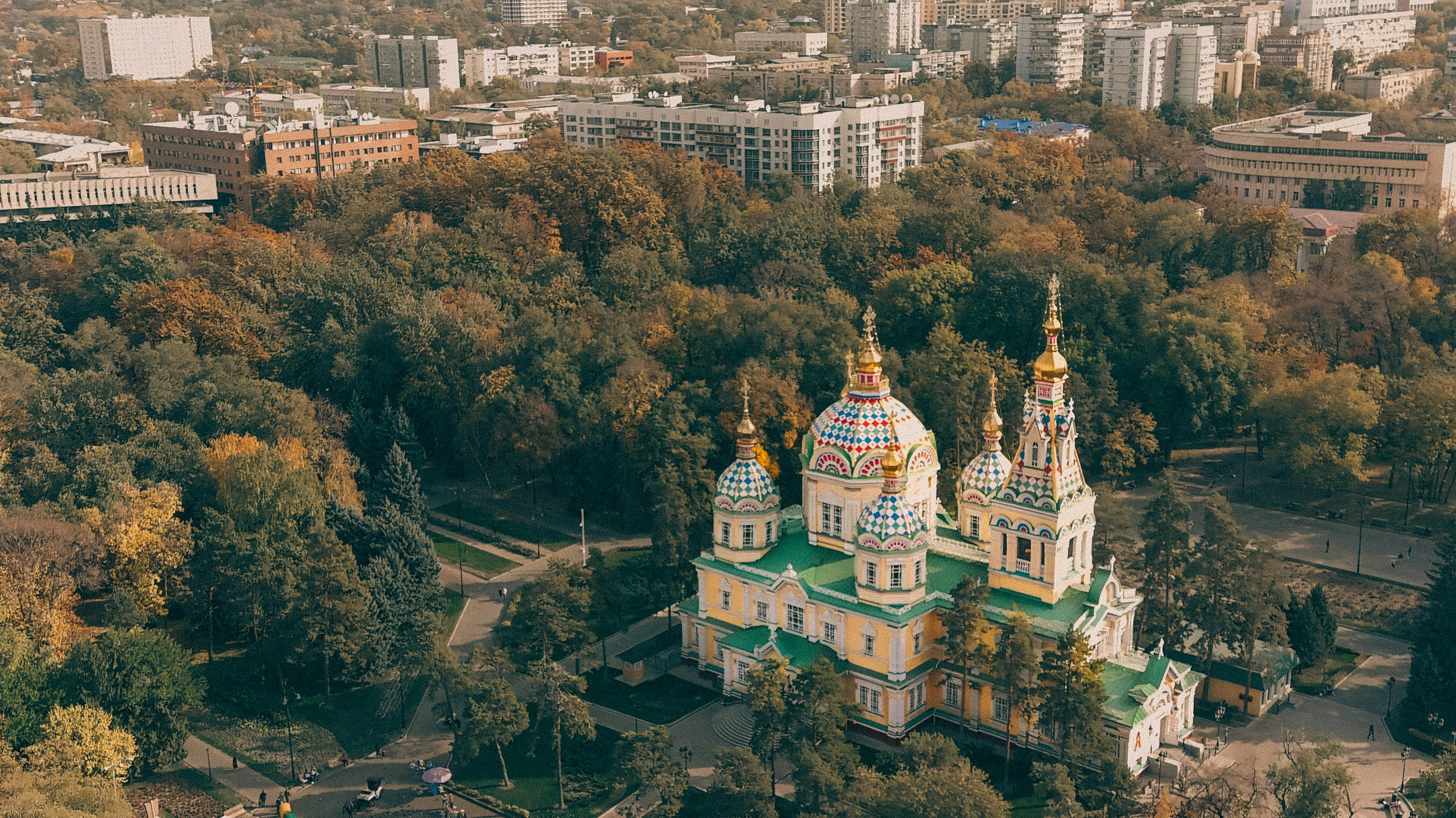 An aerial photo of Ascension Cathedral, a Russian Orthodox cathedral located in Panfilov Park in Almaty, Kazakhstan, with green park and Soviet-style buildings around