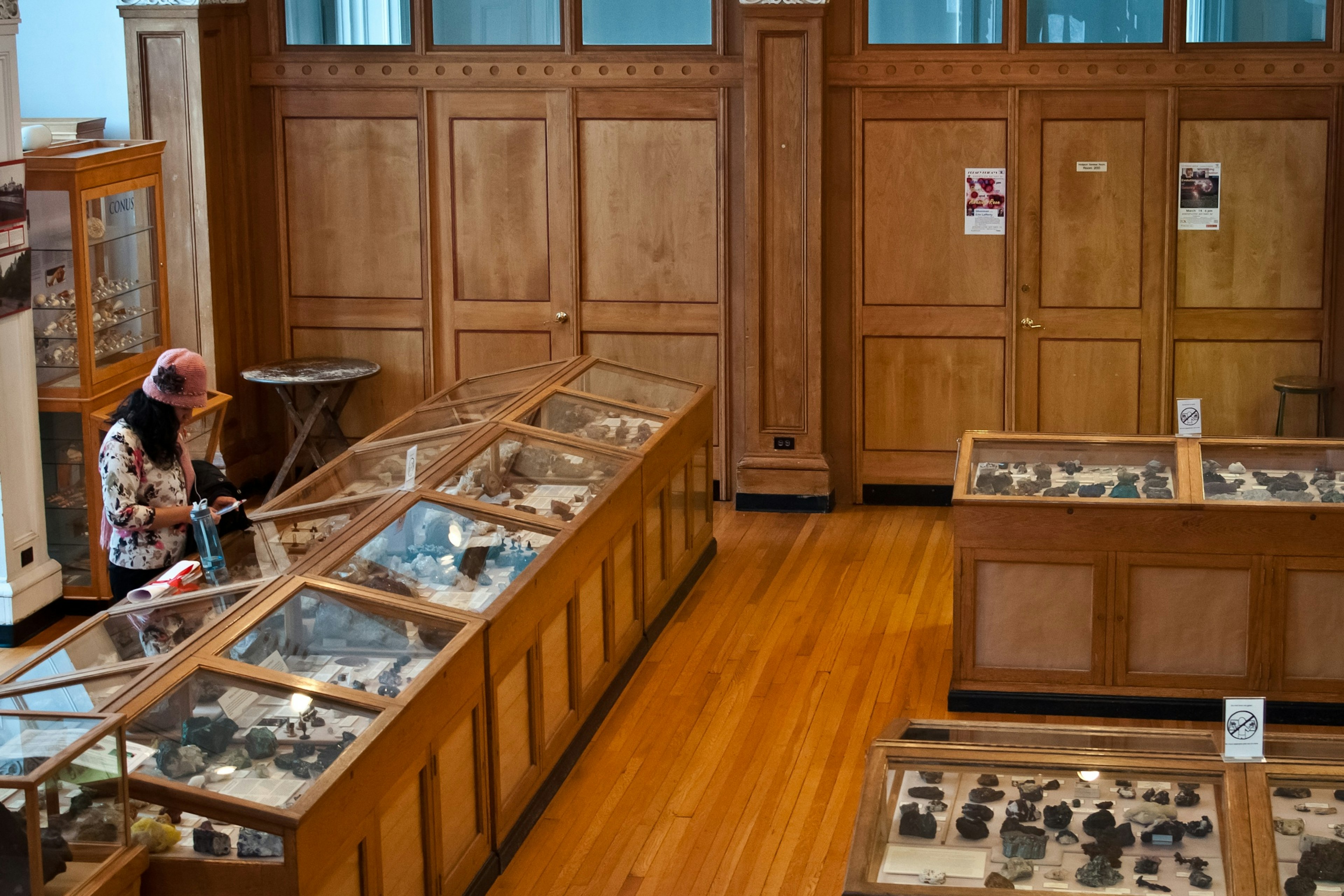 A woman looks at cabinets filled with objects in a wood-paneled gallery of the Redpath Museum, Montréal, Québec, Canada