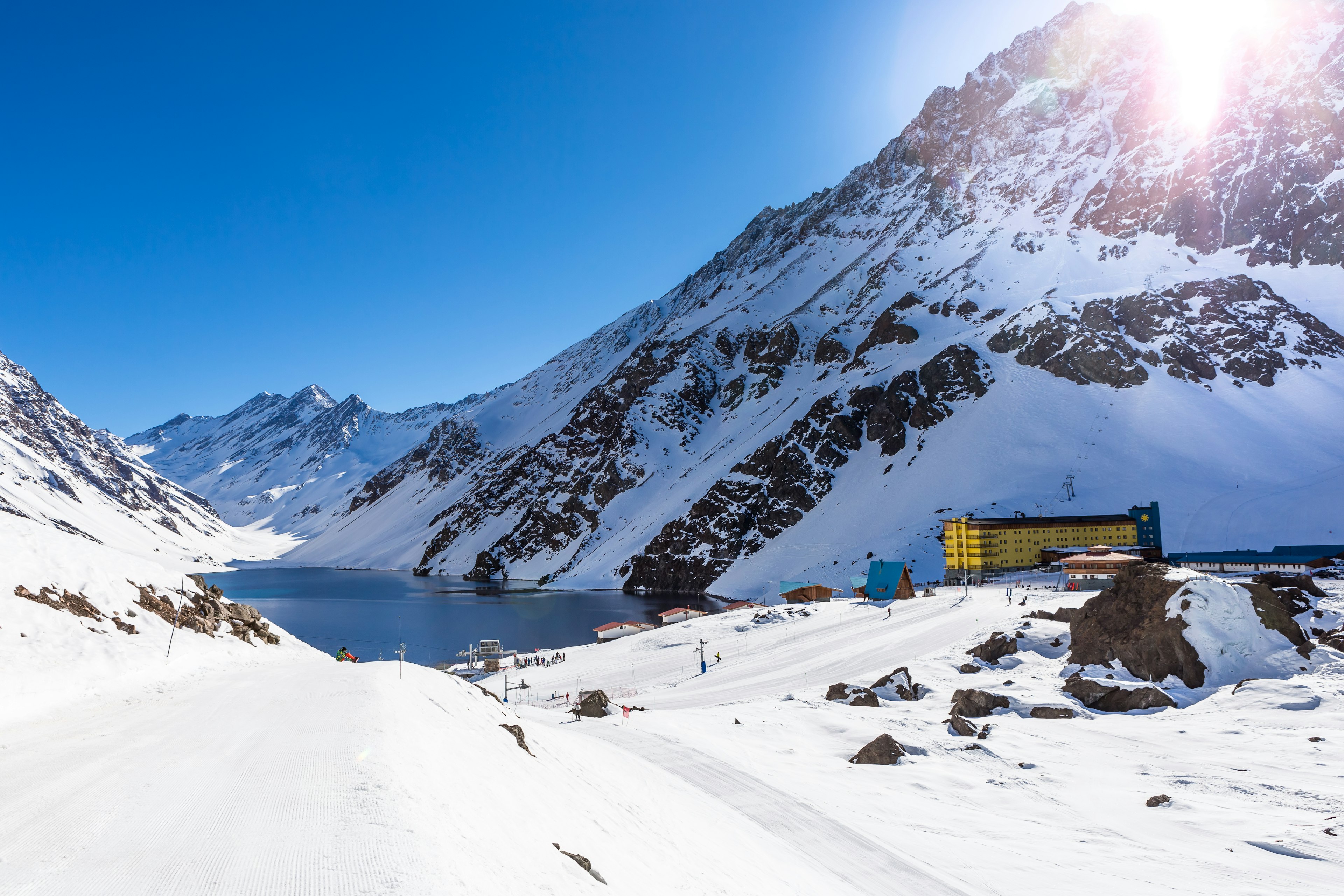 A large yellow hotel near a lake and snow-covered ski slopes