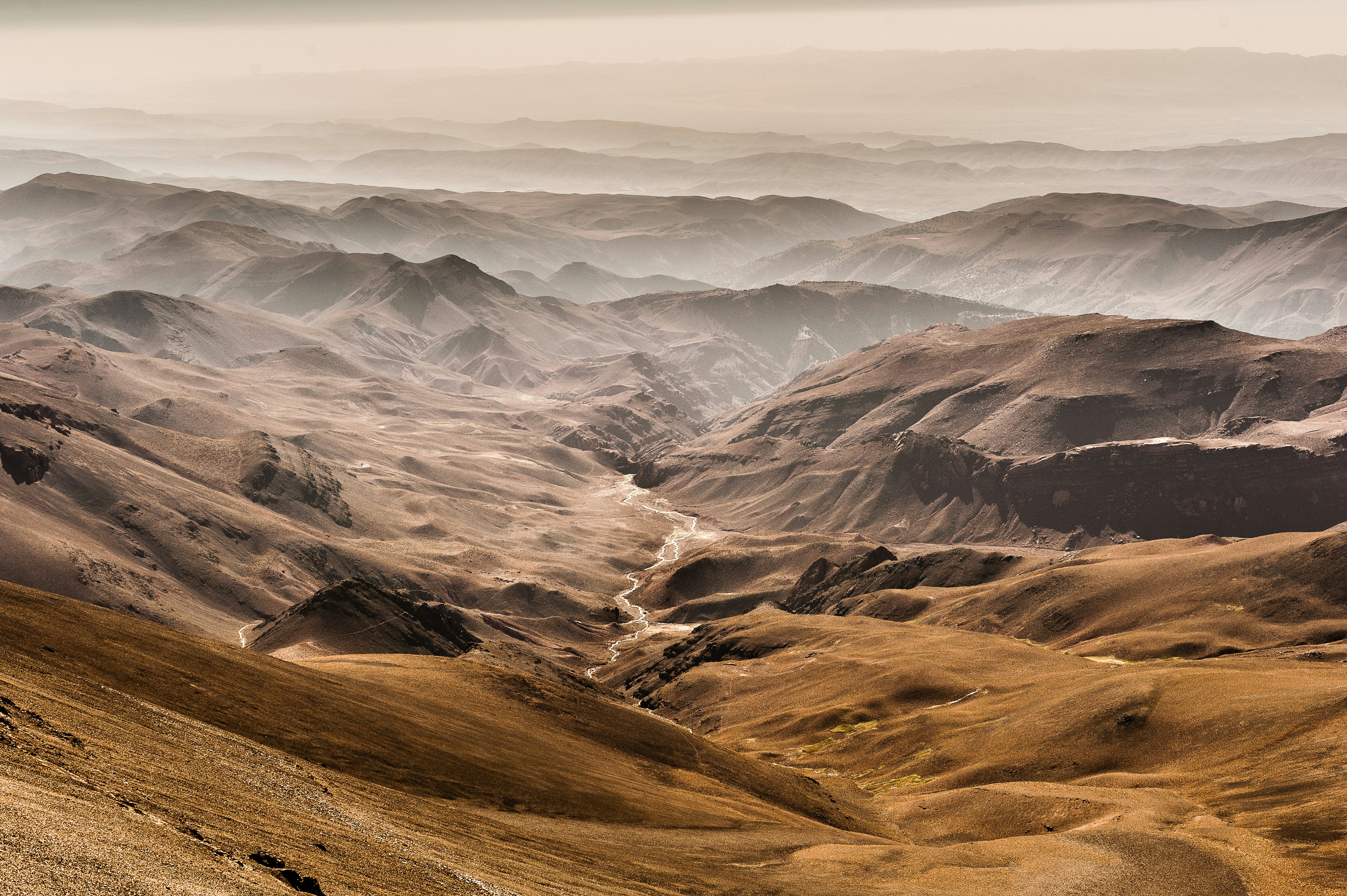 A view down over the desert-like foothills of the High Atlas Mountains; streams meander and low mist hangs in the lower valleys.