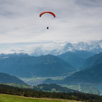 Paraglider in the Swiss Alps with snow-capped mountains in the distance.