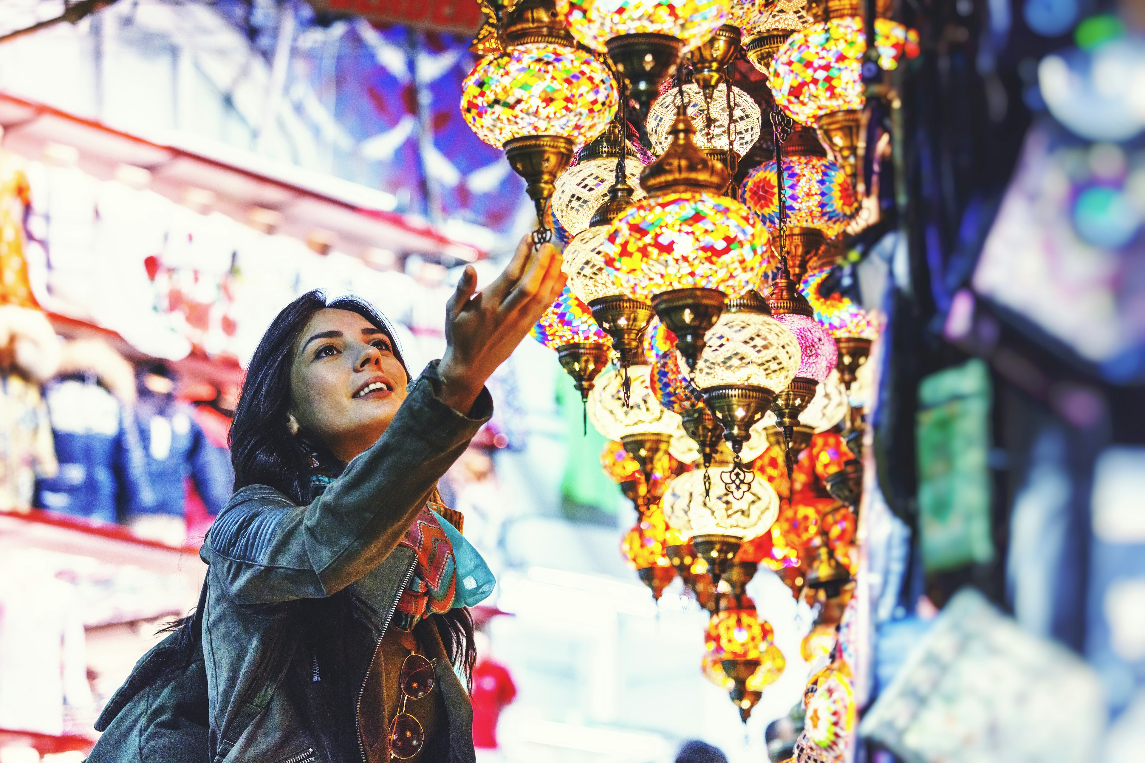 A woman lightly touches a multi-colored and ornate lantern hanging from a shop stall