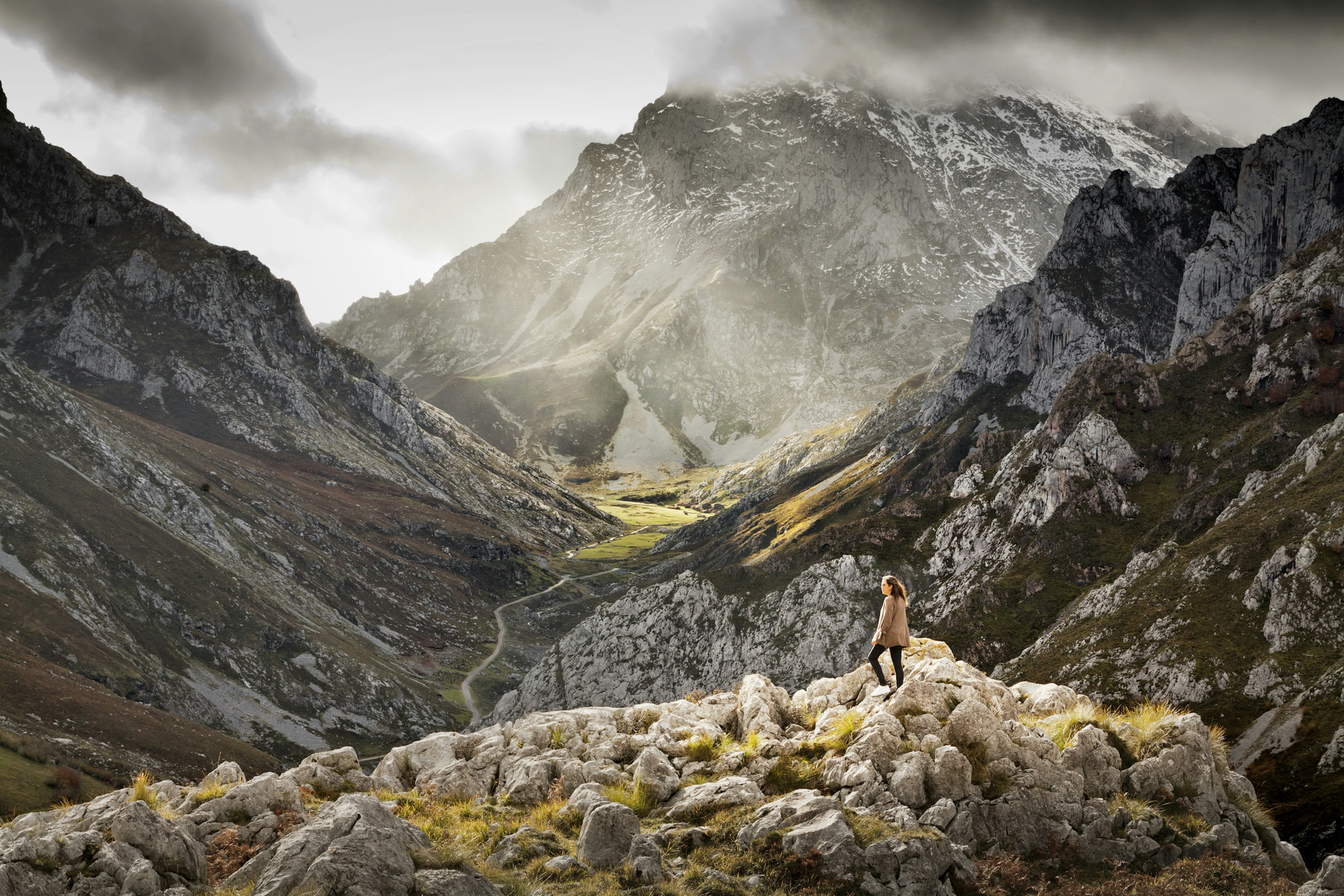 Young woman standing in front of a awe valley in Sotres, Asturias. A huge sunlit rock valley is in front of her.