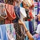 Young woman shopping for a new scarf and choosing colourful fabric in a bazaar.
