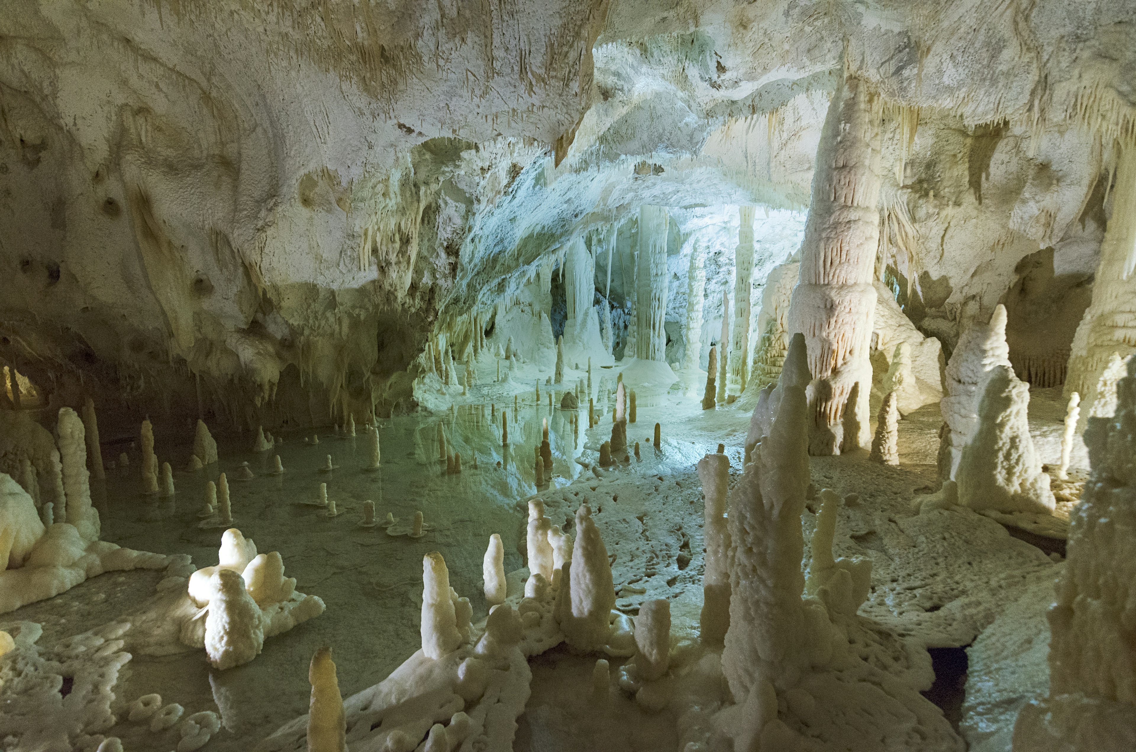 Large stone columns stretch from the floor to the ceiling of a white cavern. Grotte di Frasassi. Le Marche, Italy.