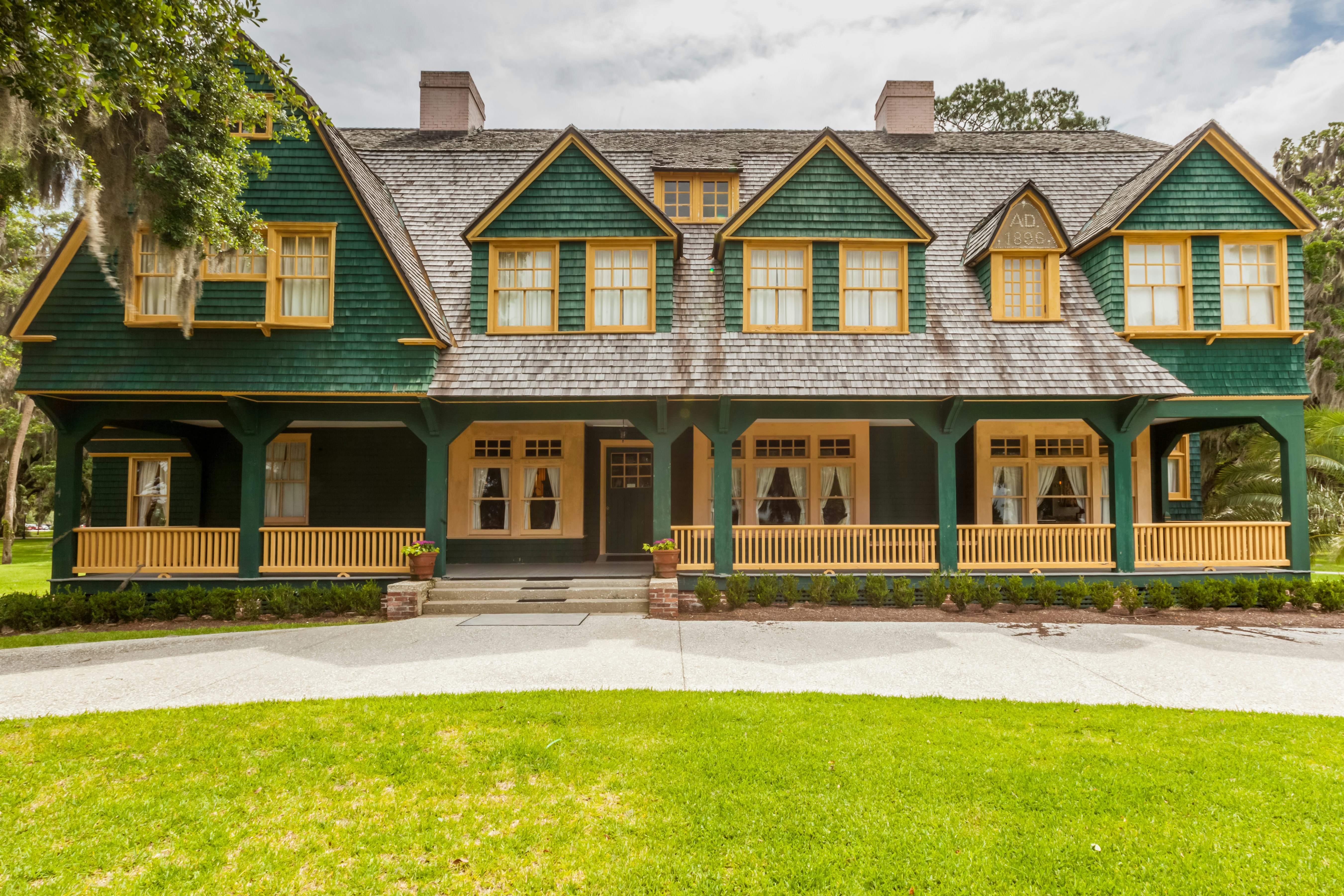 Green and yellow Cape Cod-style cottage shaded by a tree and surrounded by bright green grass on Jekyll Island