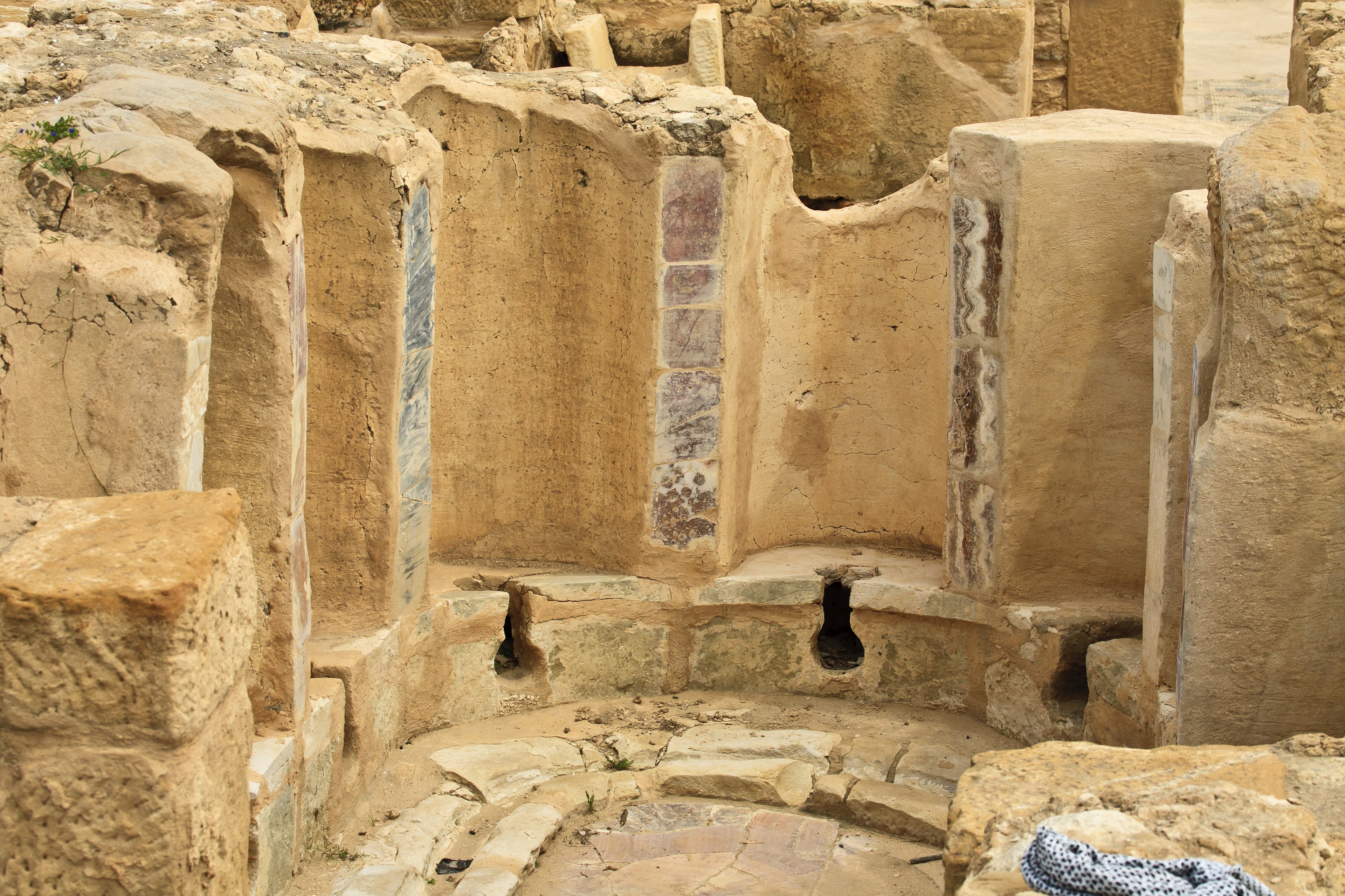 A semi-circular series of public toilets made from stone; each one has a hole in the stone seat and is backed by a curved wall.