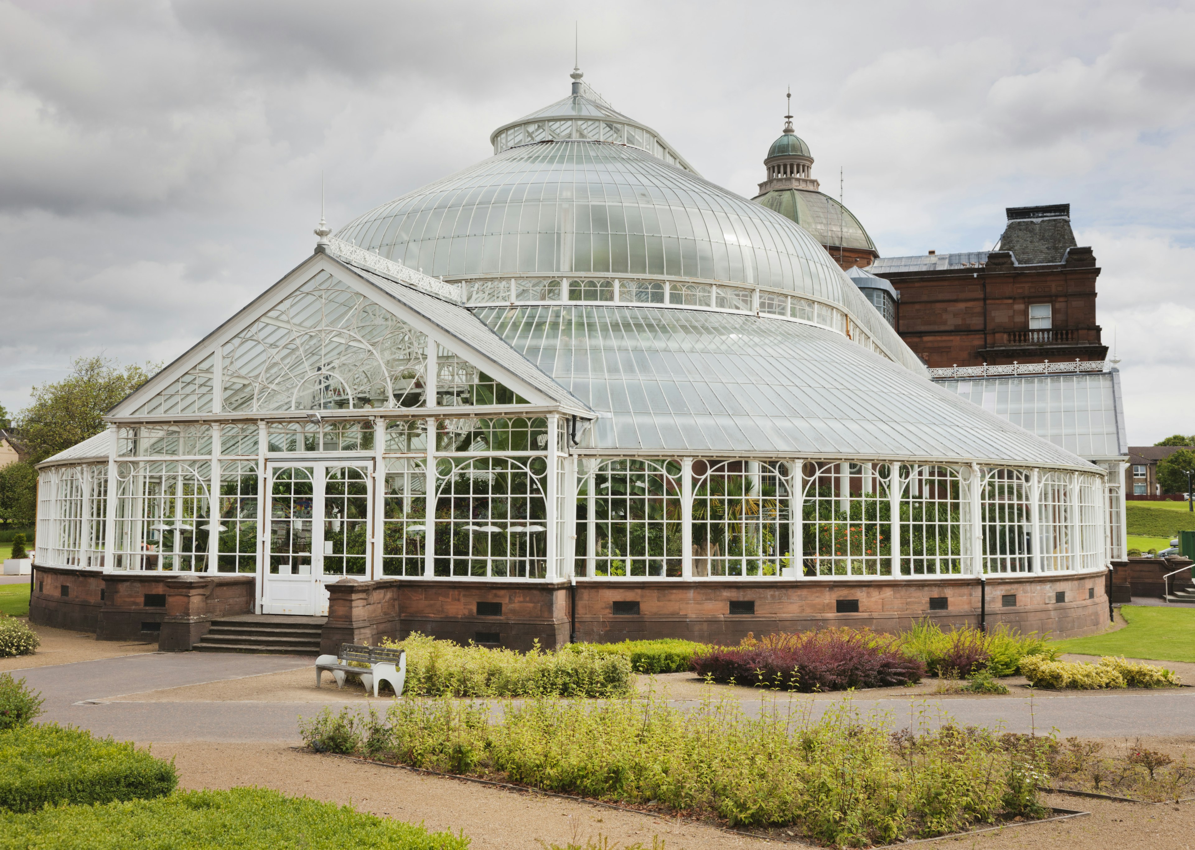 A glass gazebo surrounded by a sidewalk in the middle of a garden