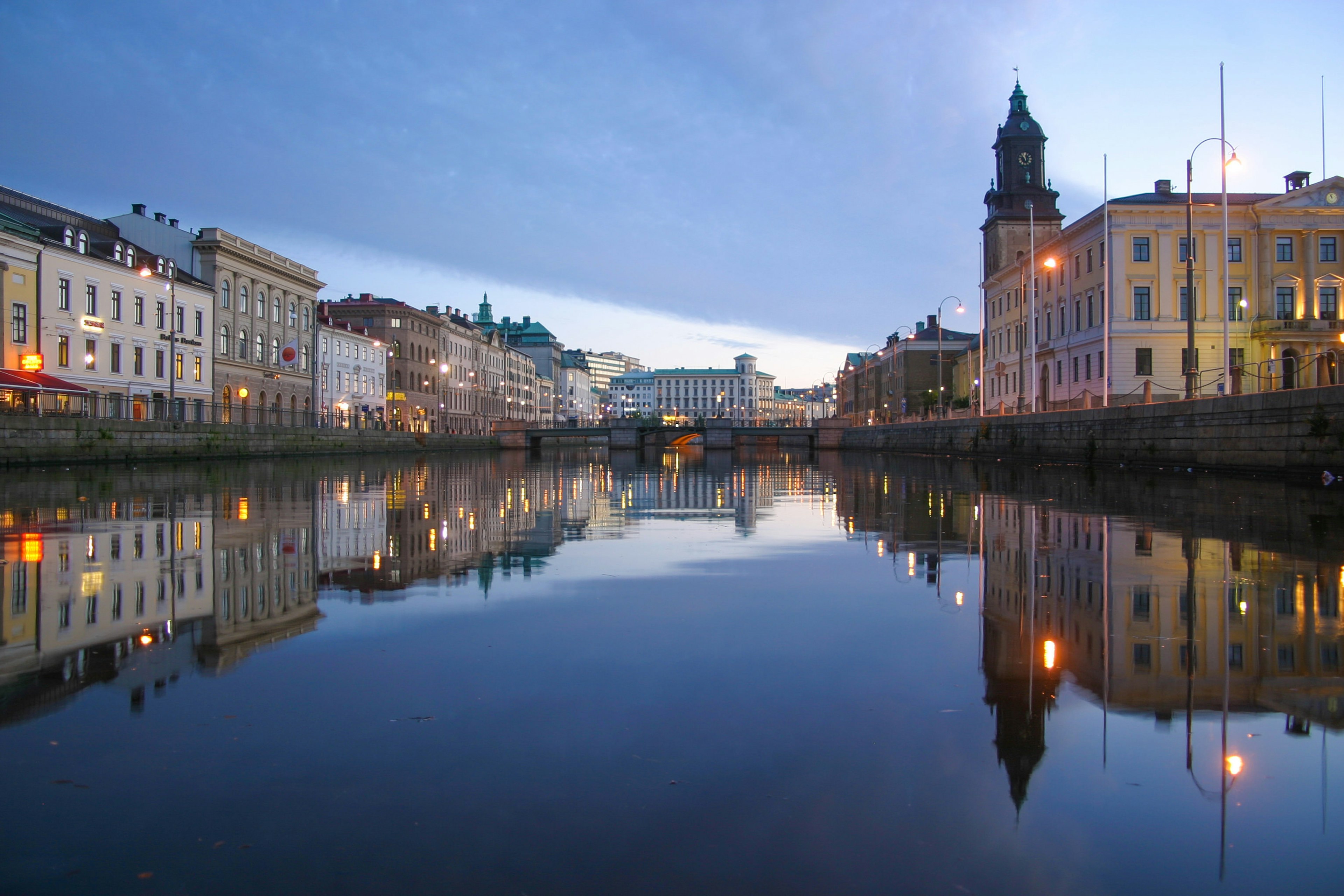 The central canal (Stora Hamnkanalen) through downtown Gothenburg, buildings reflected in the water. streetlights illuminate a dusk evening.