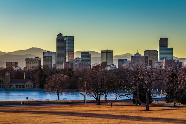 Parkland gives way to a river and a city. In the distance is a range of mountains
