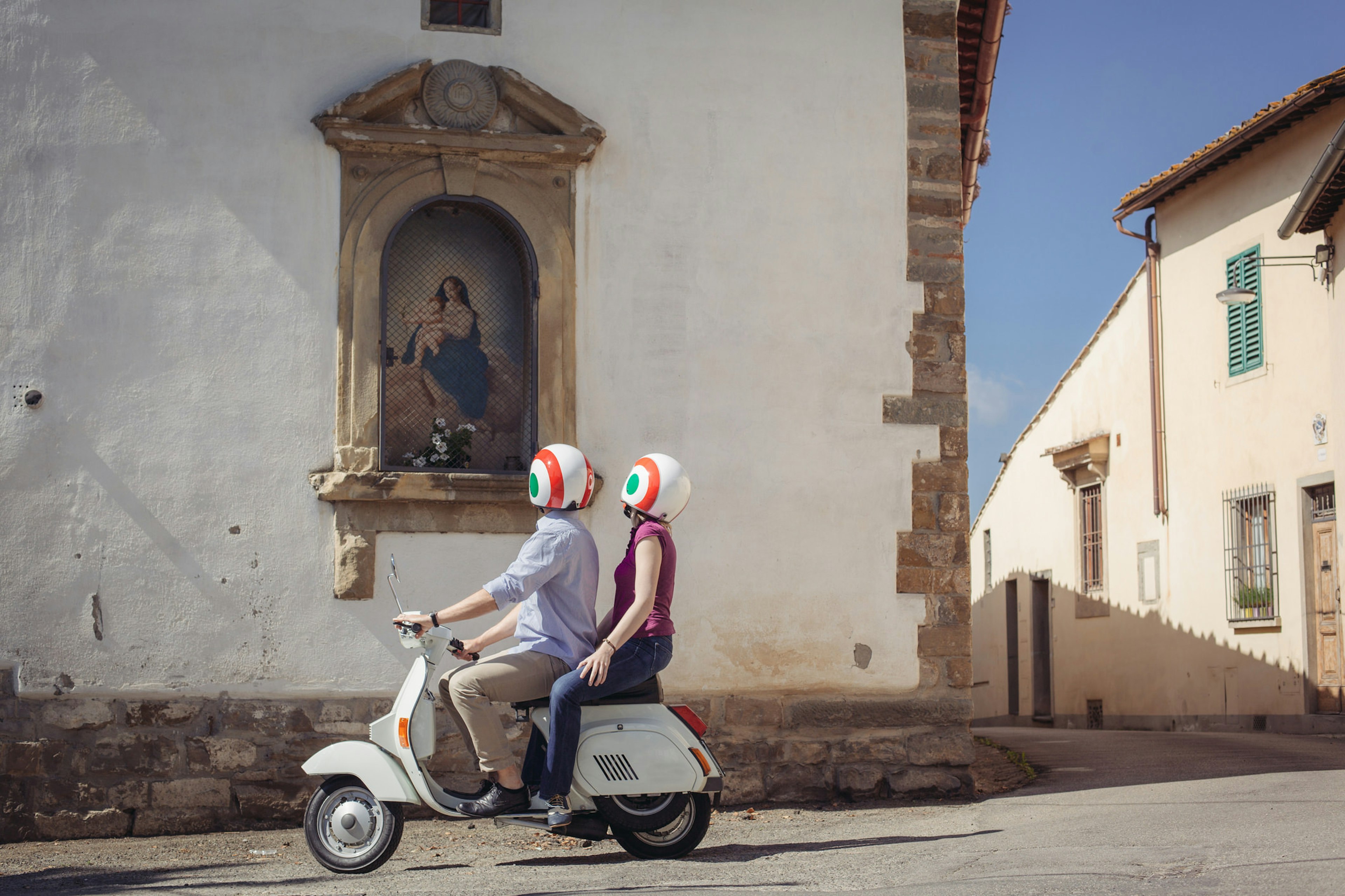 A couple on a scooter stop to look up at mural on the wall.