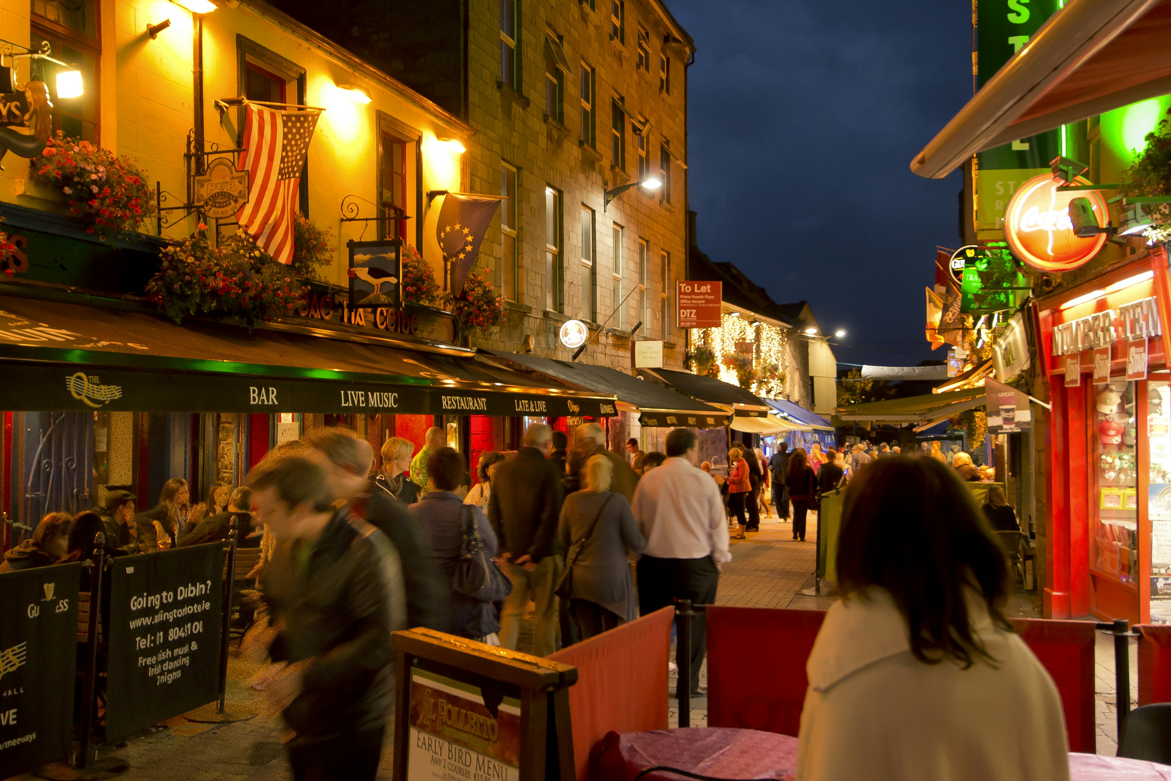 People walking along a street lined with pubs at night in Galway.