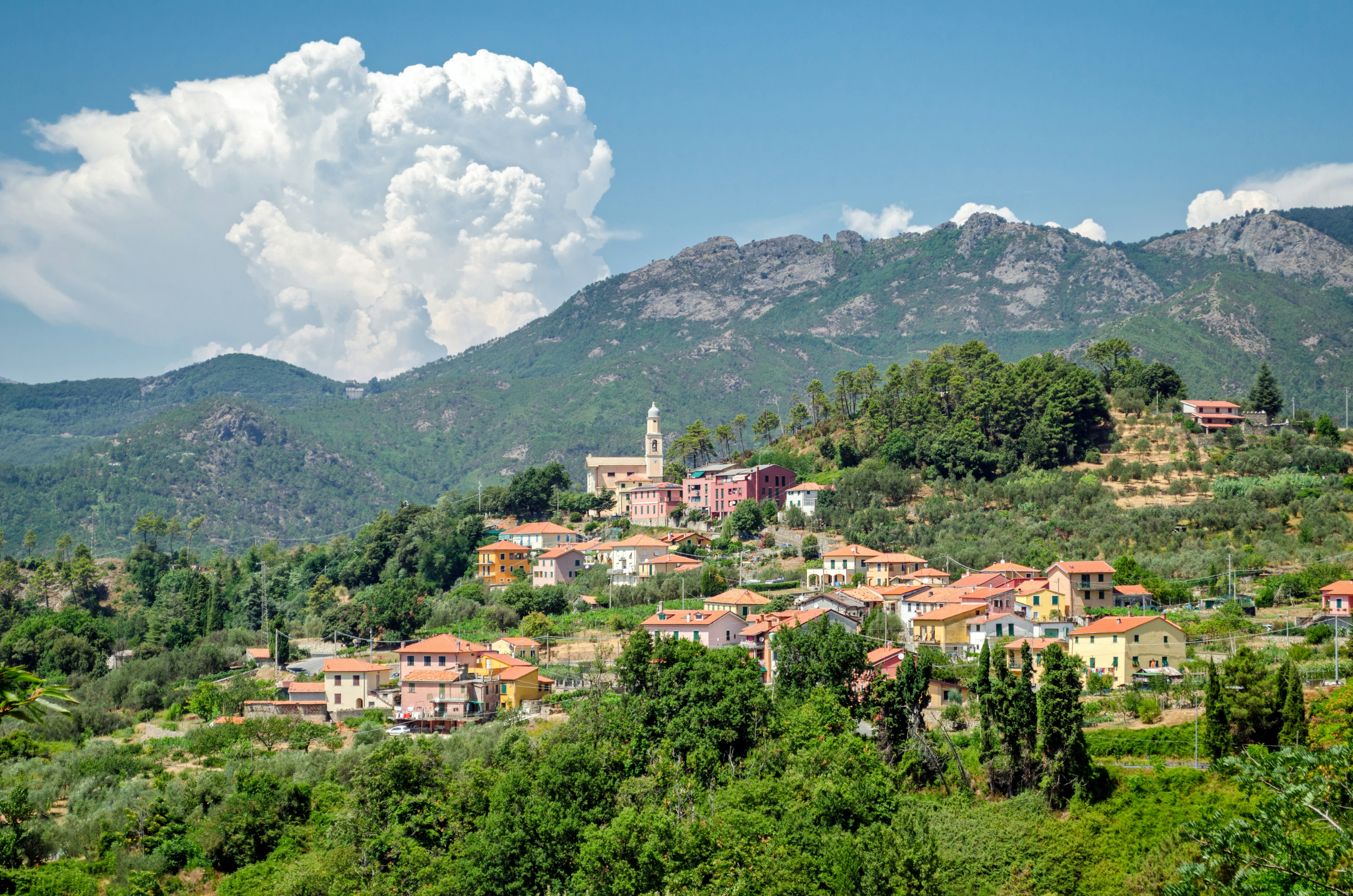 The pastel-coloured buildings of one of Framura's hamlets sit on a hillside, with taller hills behind