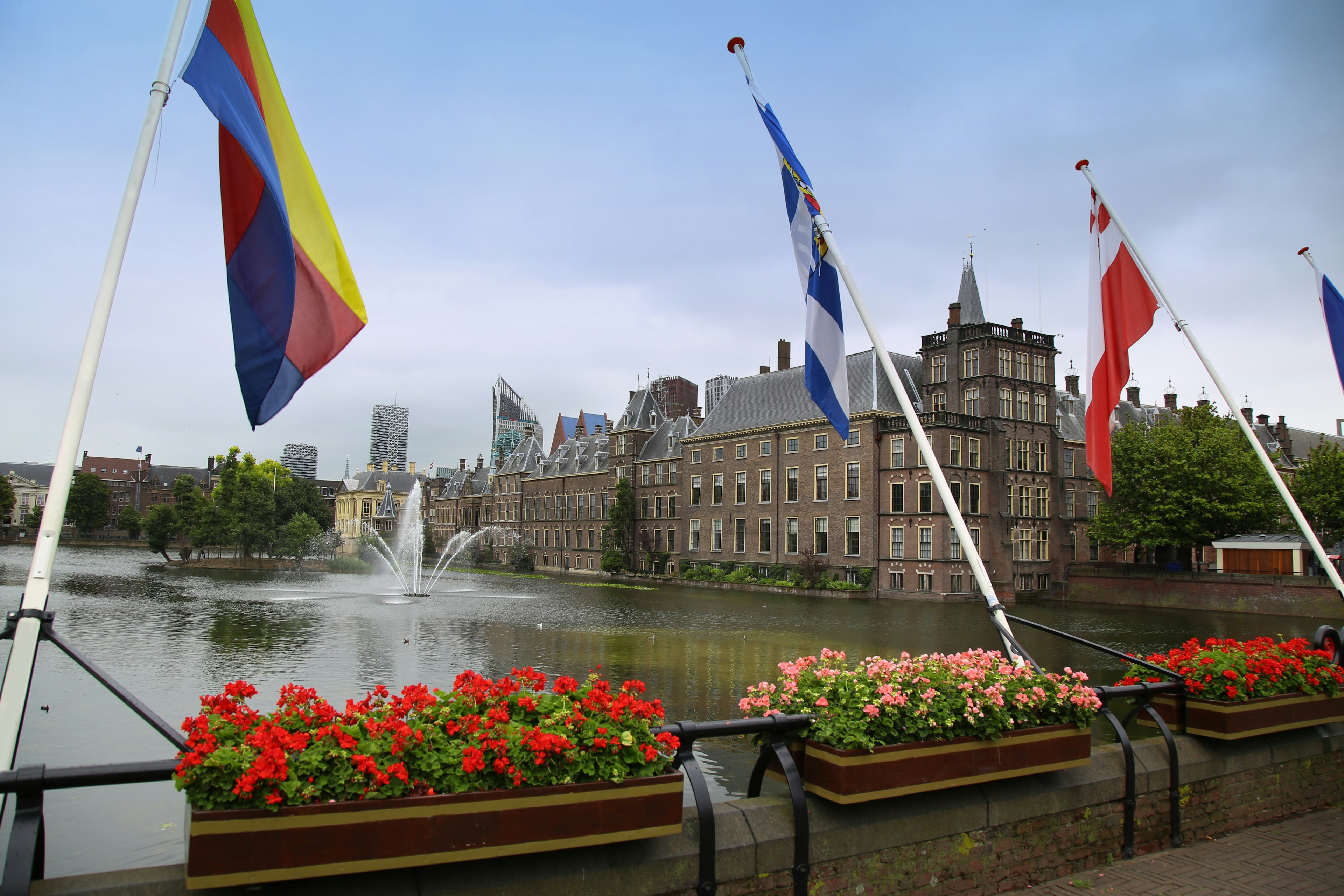 Binnenhof Palace, Dutch Parlament in the Hague, Netherlands. Many flags in the foreground in front of a lake with a fountain.