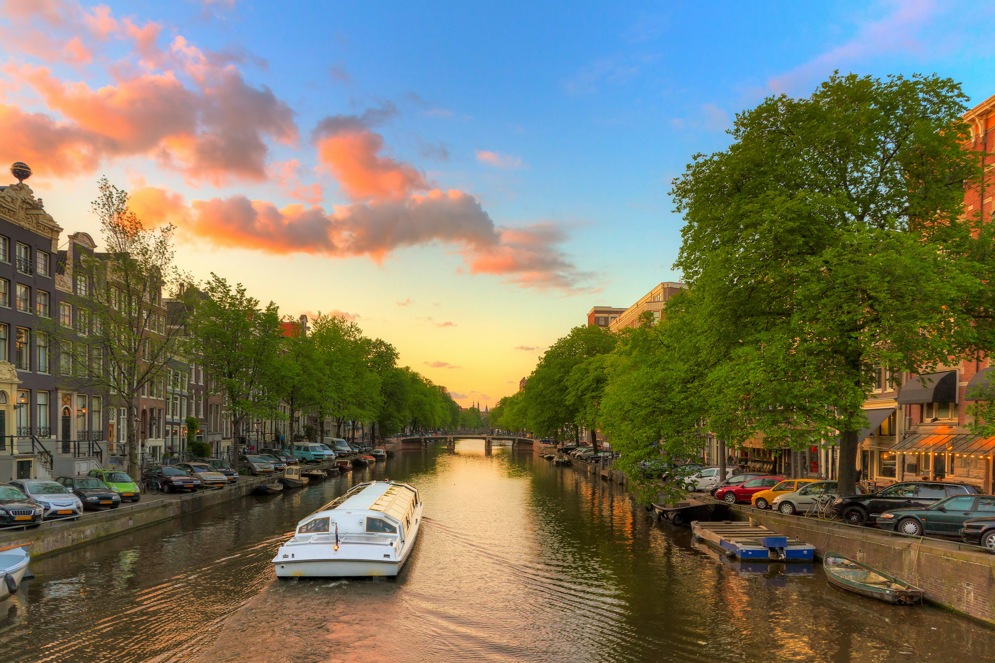 A boat heading down an Amsterdam canal at sunset.