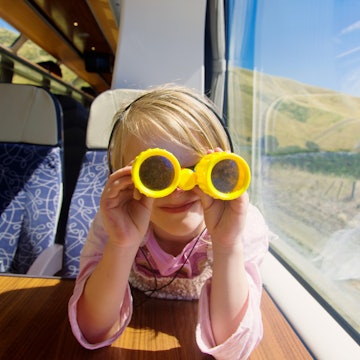 Young girl enjoying a coastal train trip with yellow binoculars.