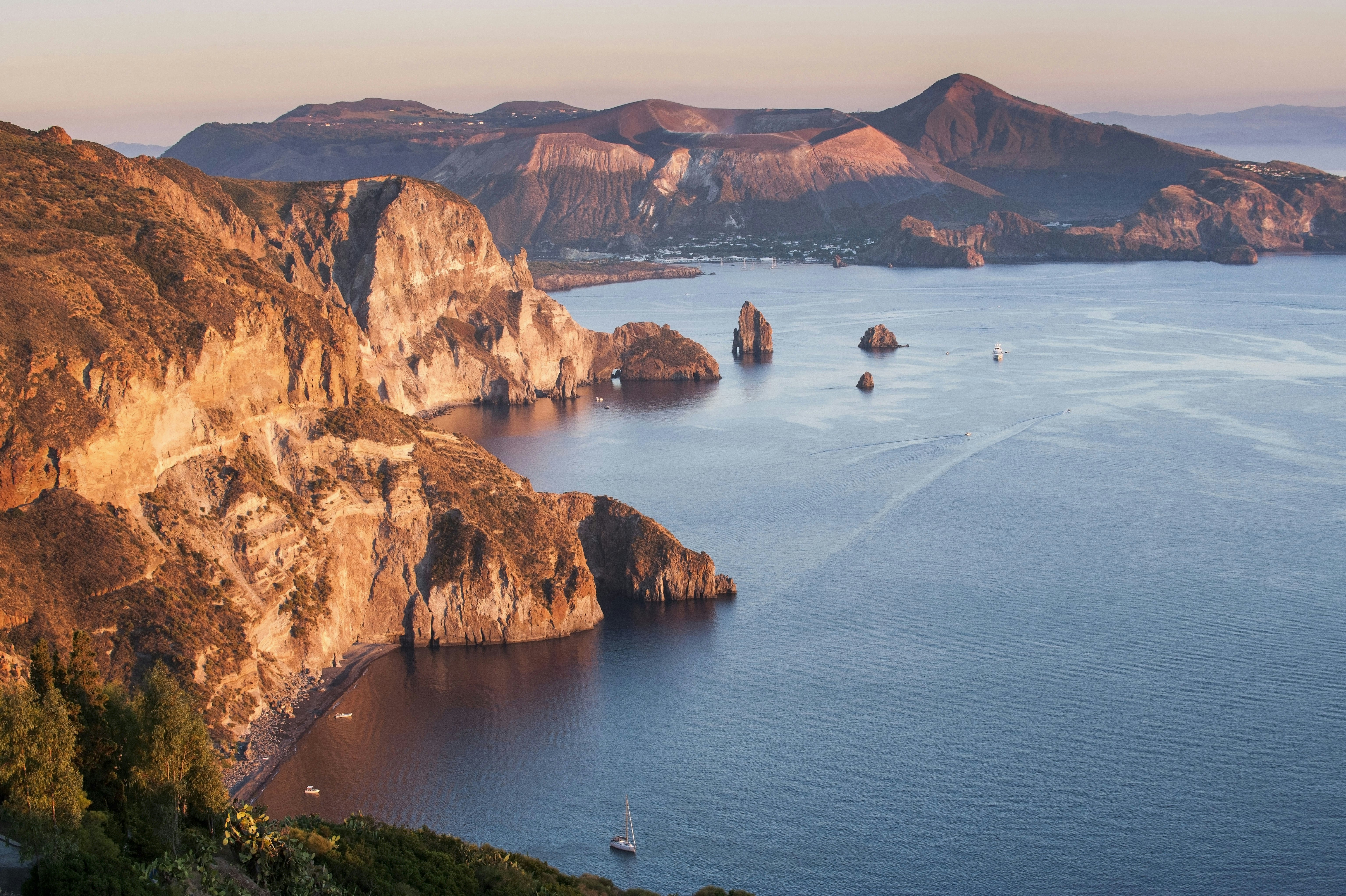 A volcanic coastline of cliffs with boats sailing by.