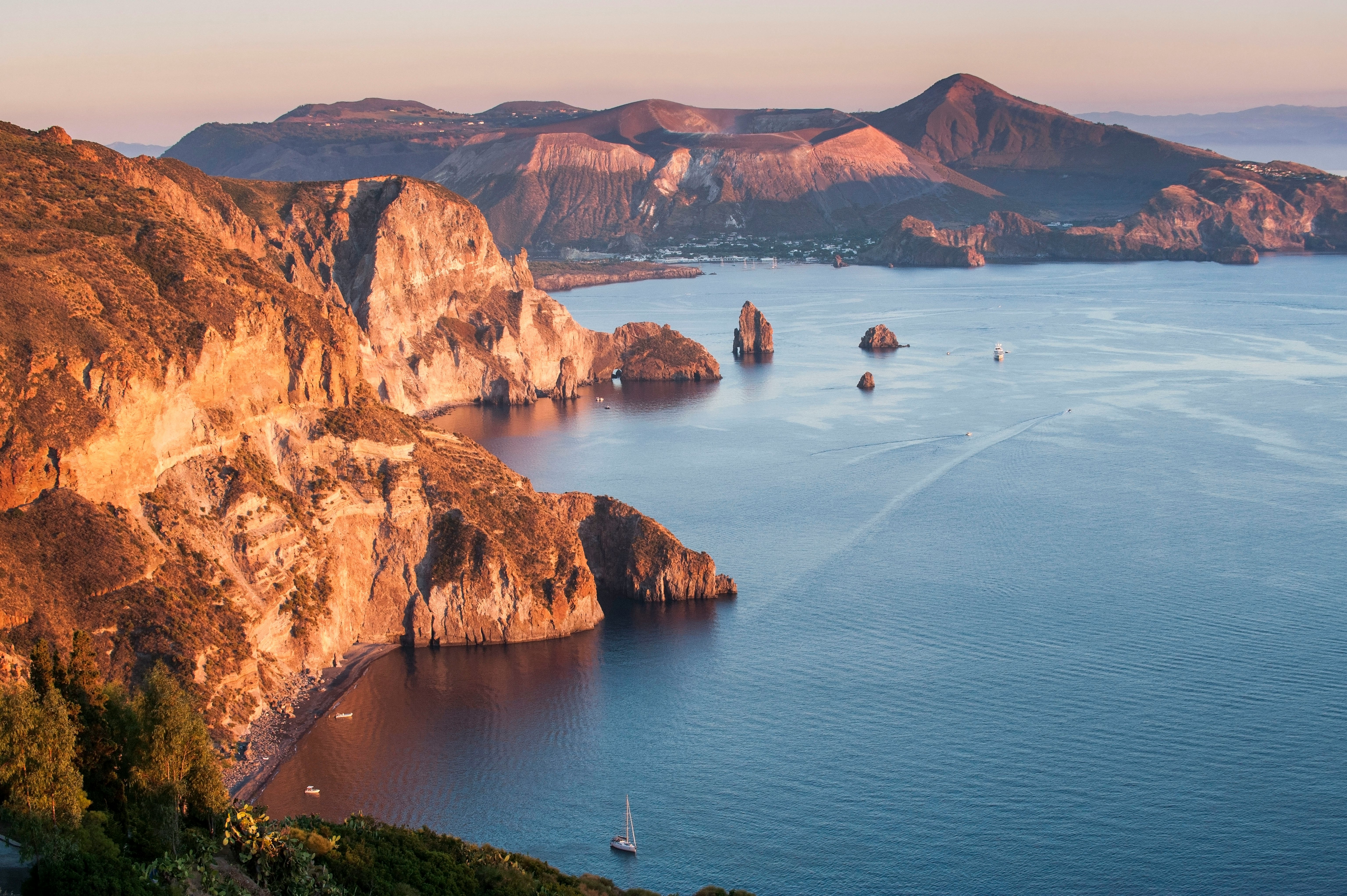 A volcanic coastline of cliffs with boats sailing by.
