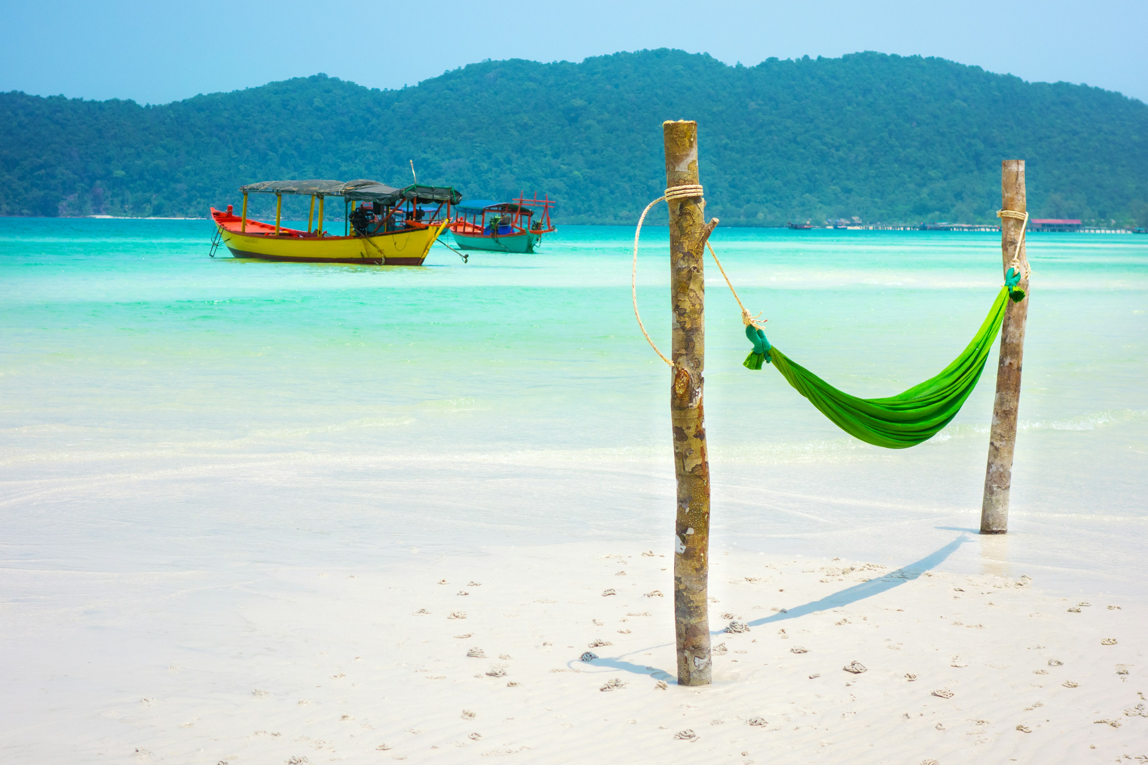 A hammock on the beach of Koh Rong Samloem, with two boats anchored off shore.