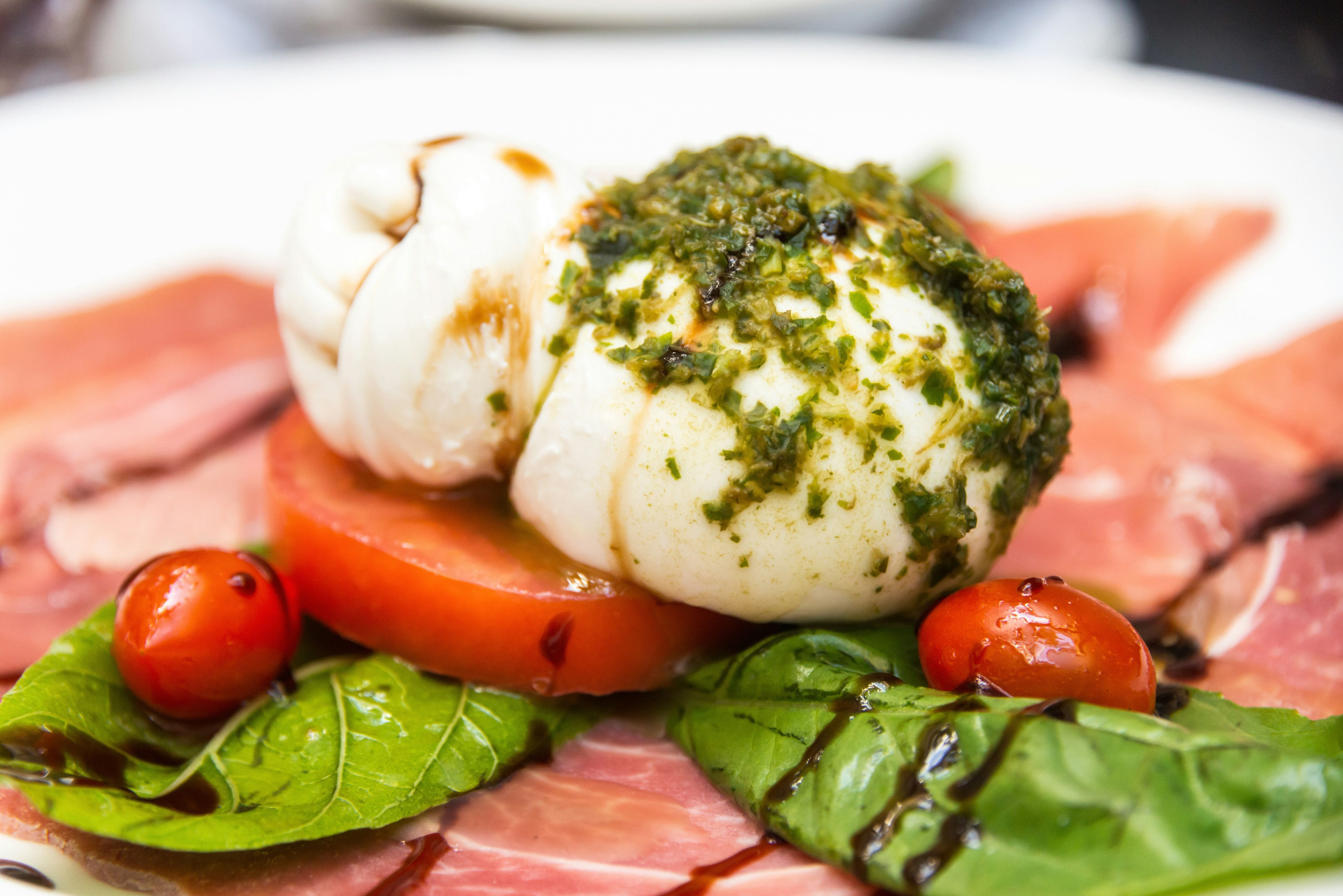 A ball of white cheese sits on top of tomato and a cured meat.