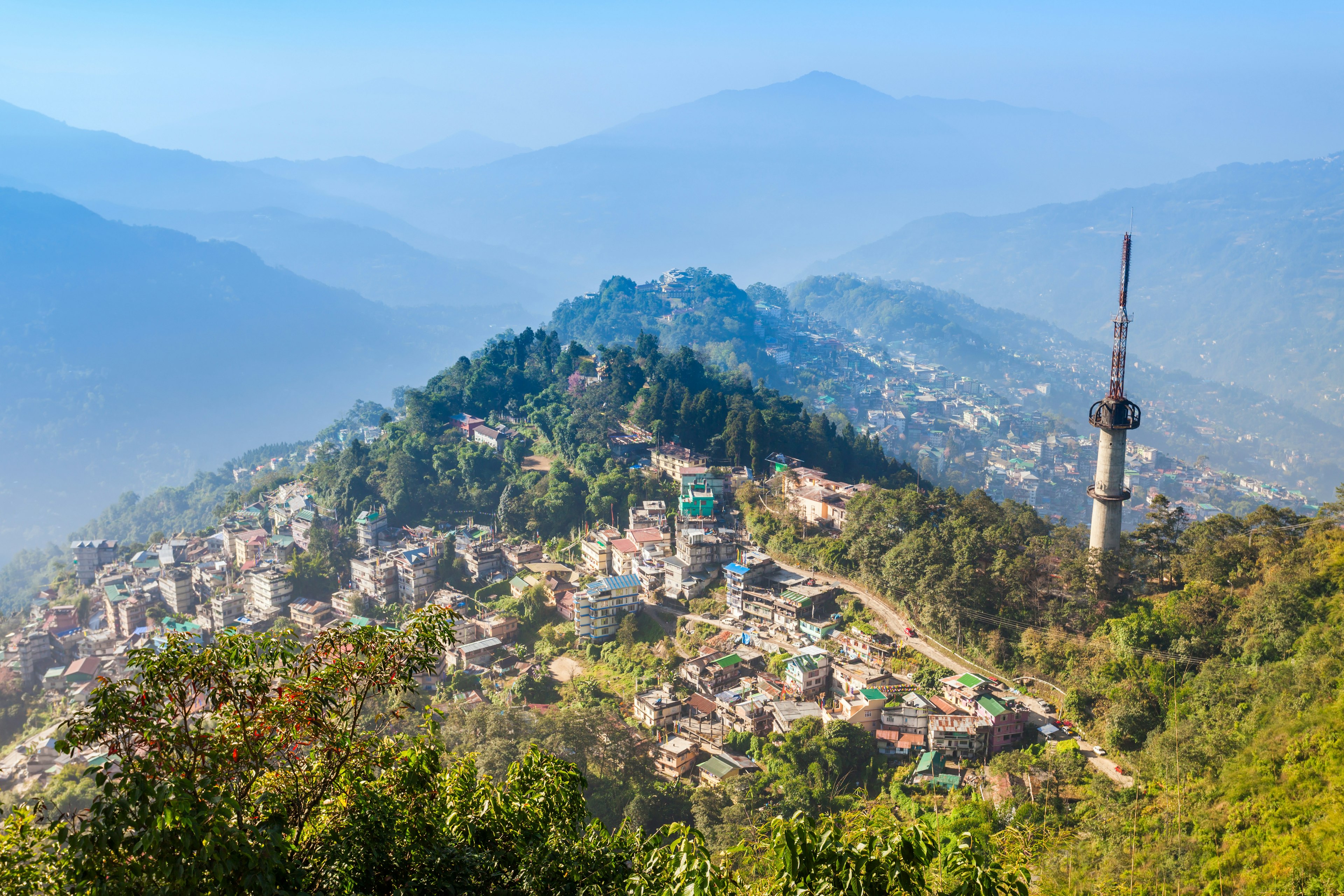 A small city spread out on hillsides and mountain peaks surrounded by green foliage