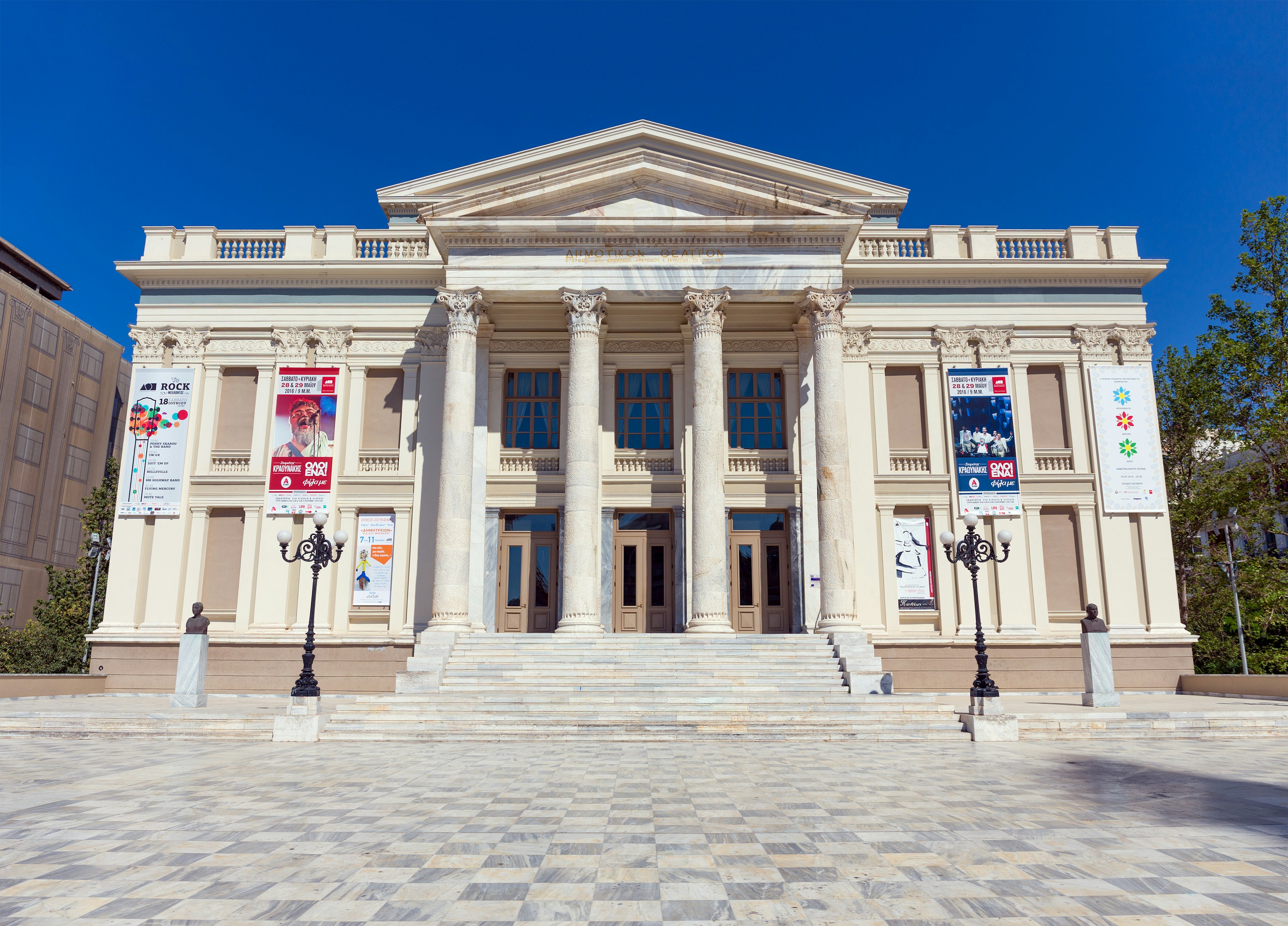 A neoclassical theater house sits in a plaza with checked stones. Piraeus, Greece.