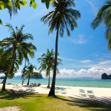 A beautiful beachscape surrounded by palmtrees, the ocean spreads out to the distance where islands decorate the horizon.