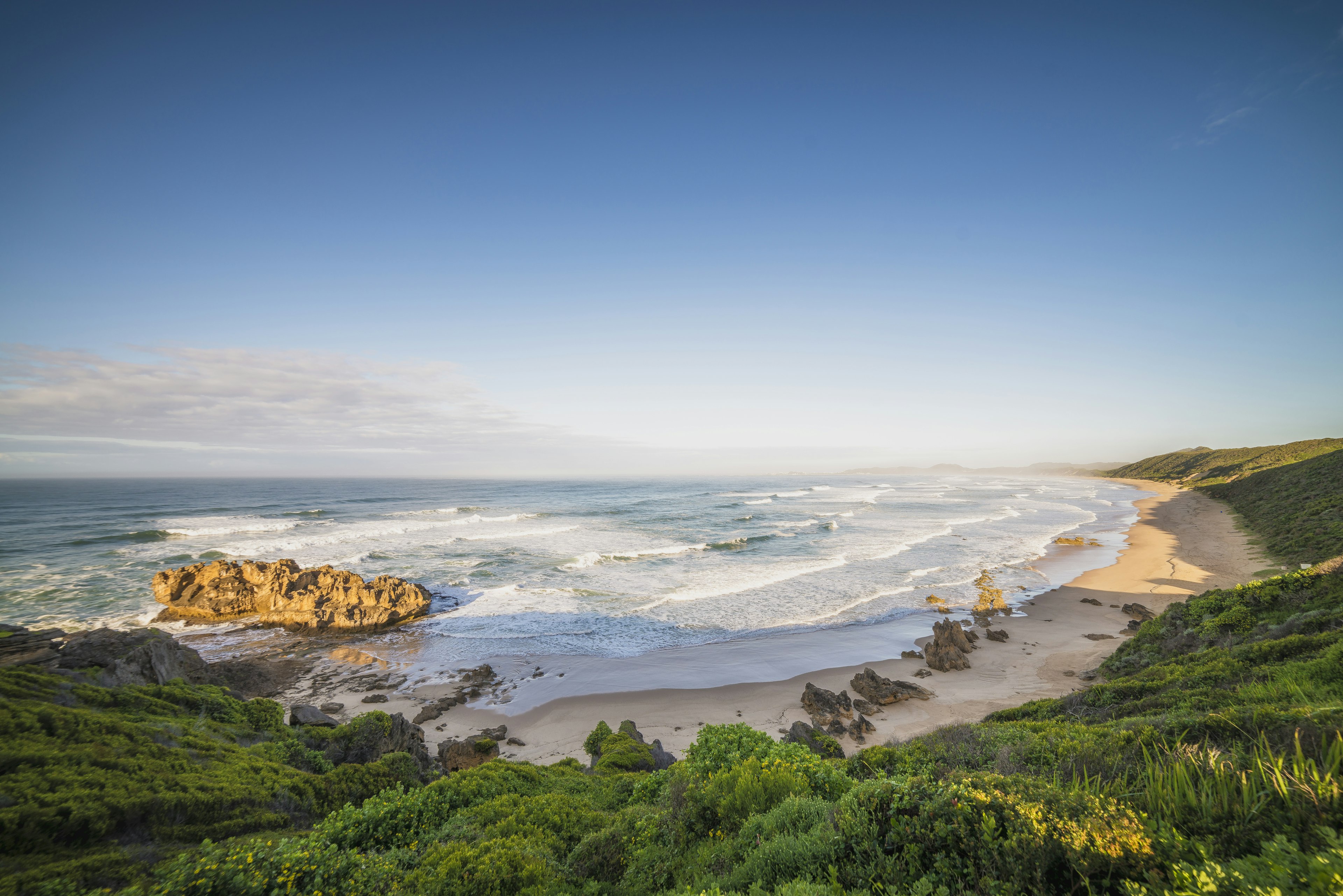 A long curve of sand backed by lush hills is pounded by waves