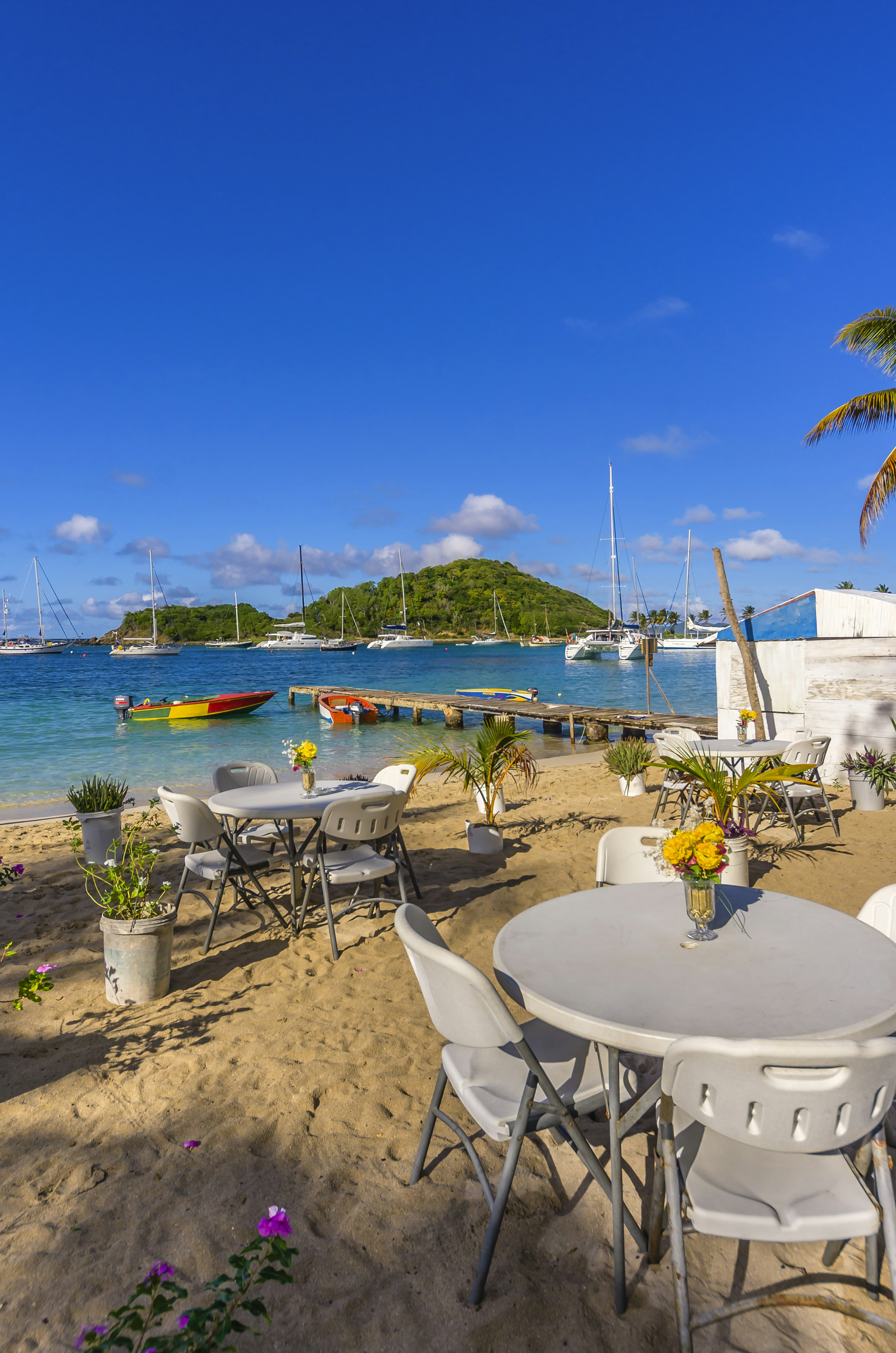 Enjoy a seaside cocktail on Mayreau. Tables on the beach with flower arrangements, boats and islands in the background of a beach scene.