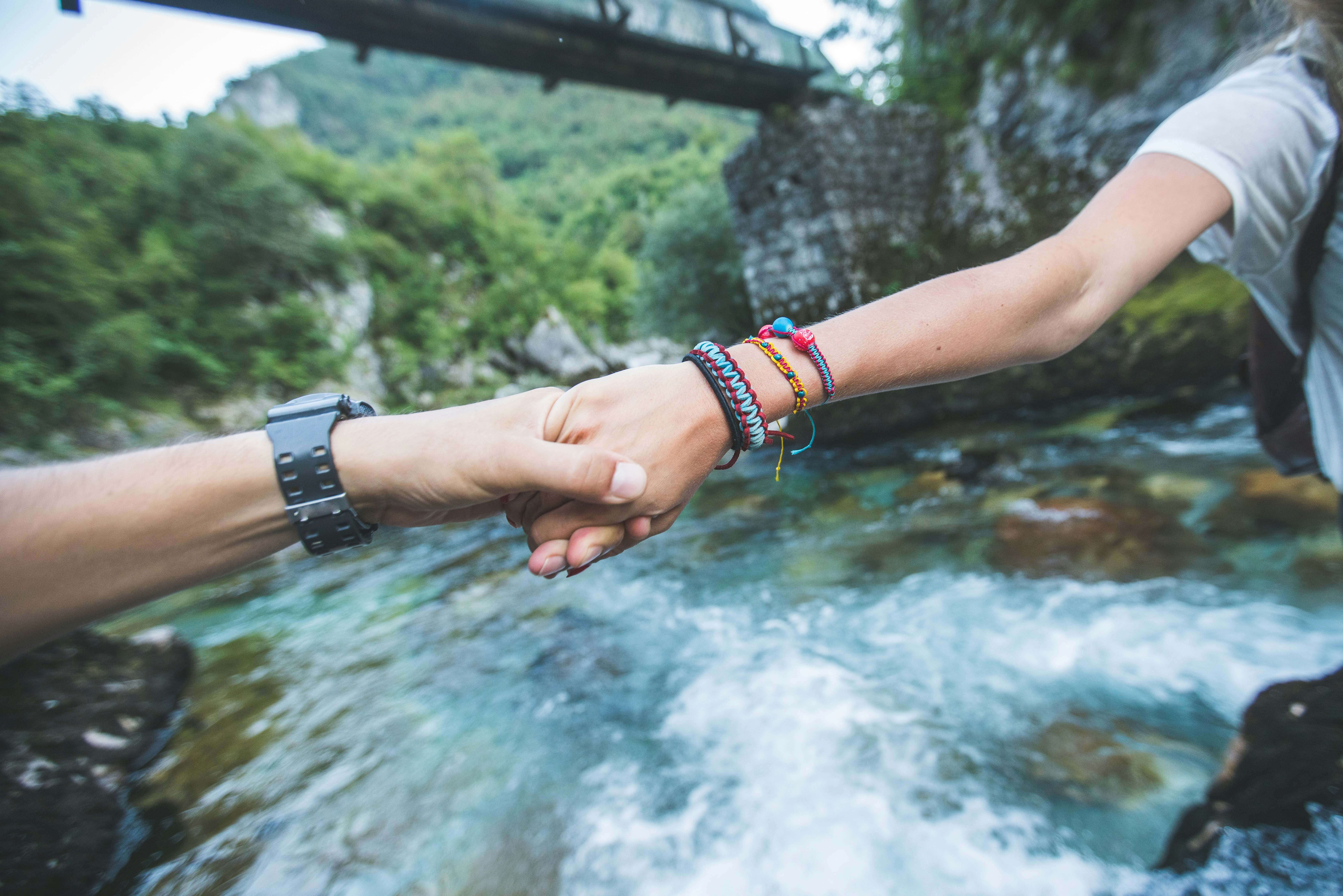 Travellers holding hands as they cross a river.