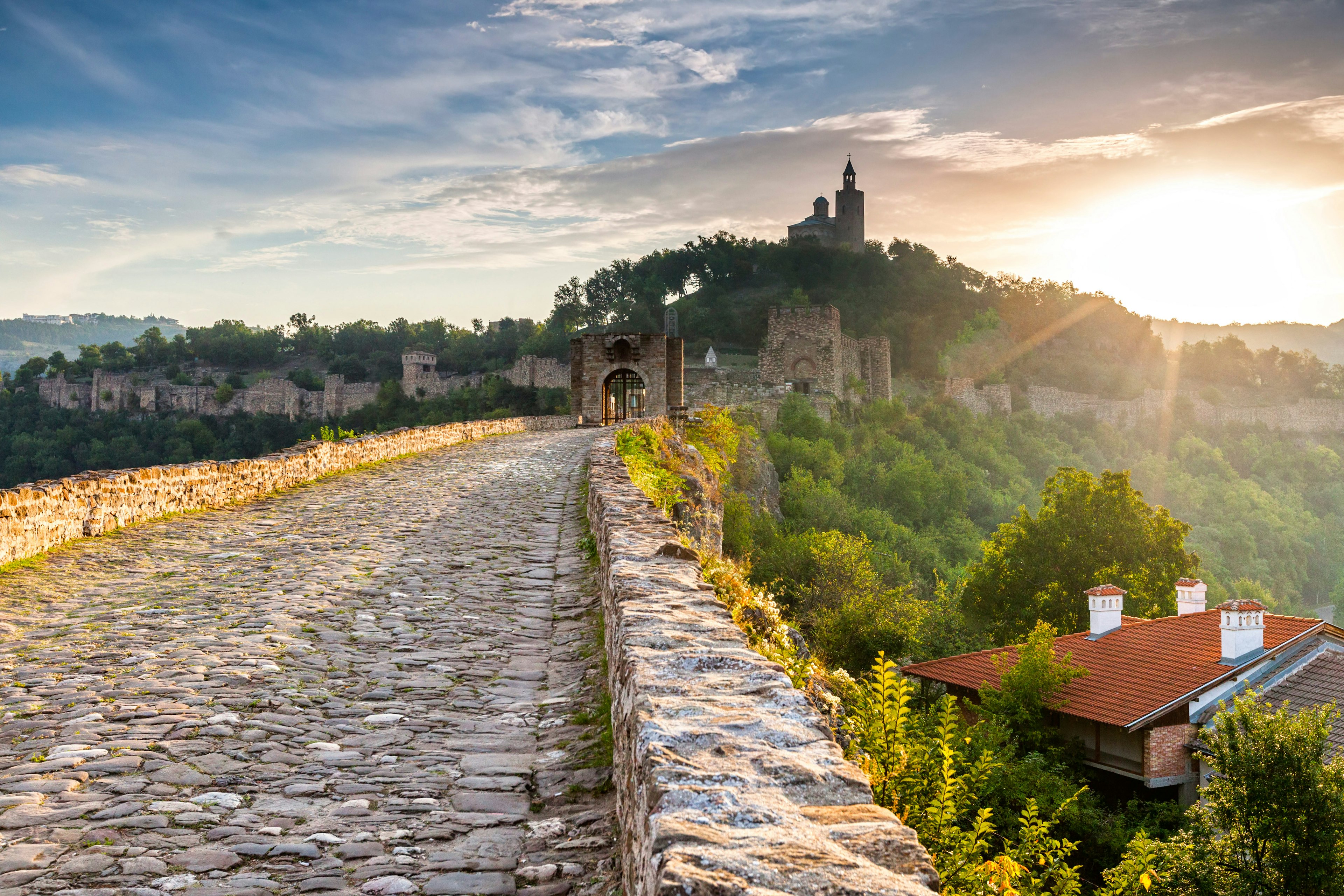 A cobbled lane leads to a medieval walled fortress in the distance